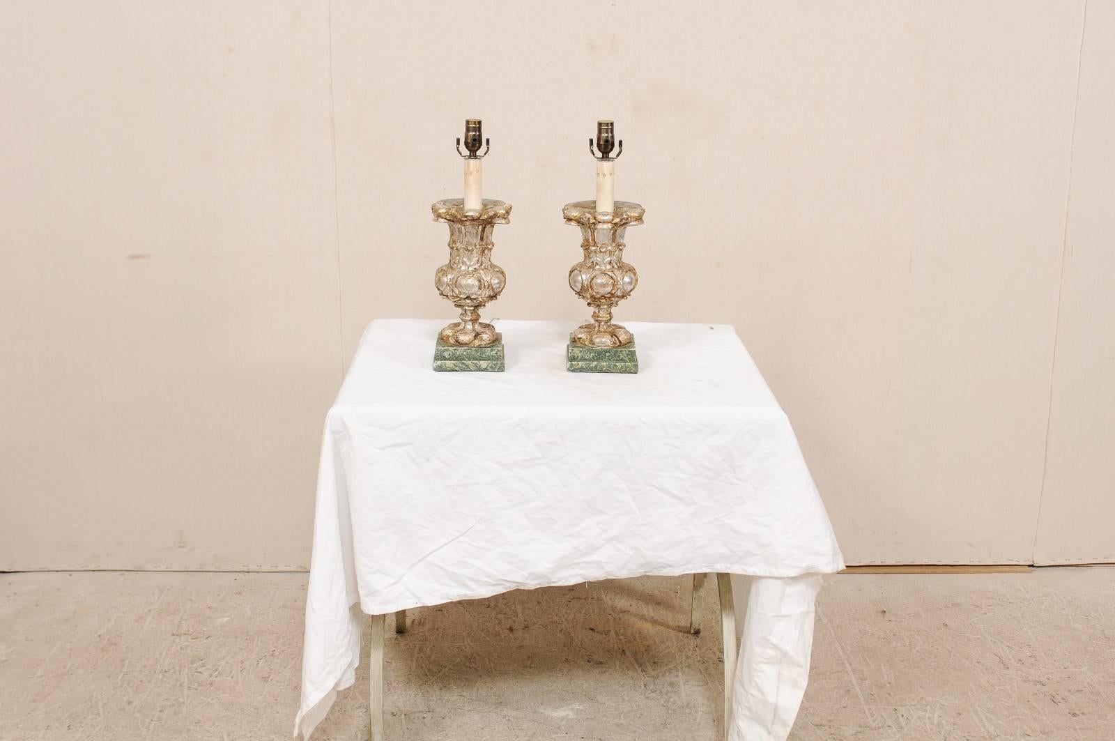 A pair of 19th century Italian table lamps. This pair of antique Italian carved wood table lamps feature urn shaped bodies raised upon a squared base. The urn bodies have hand-carved details about their fronts with leaf and convex circular motifs,