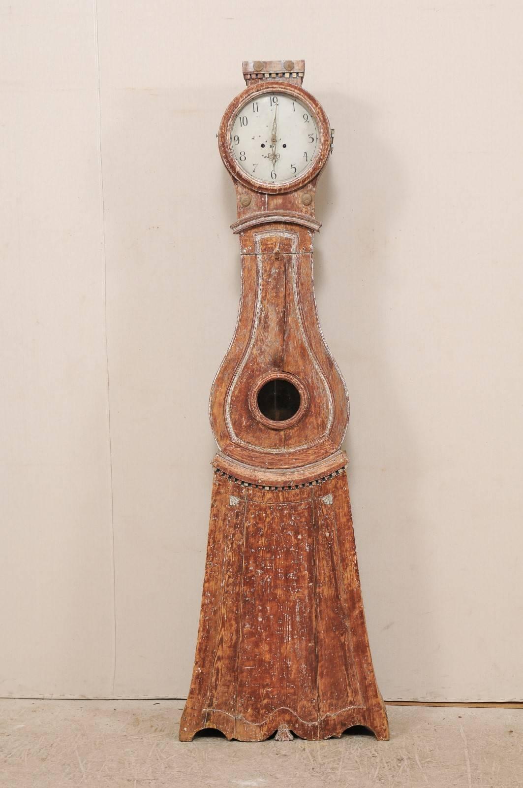 A 19th century painted wood Swedish clock. This Swedish clock from the 1820s features a raised flat-top crest, its original round metal face and movements, a raindrop shaped belly and triangular bottom. There are carved dentil accents about the