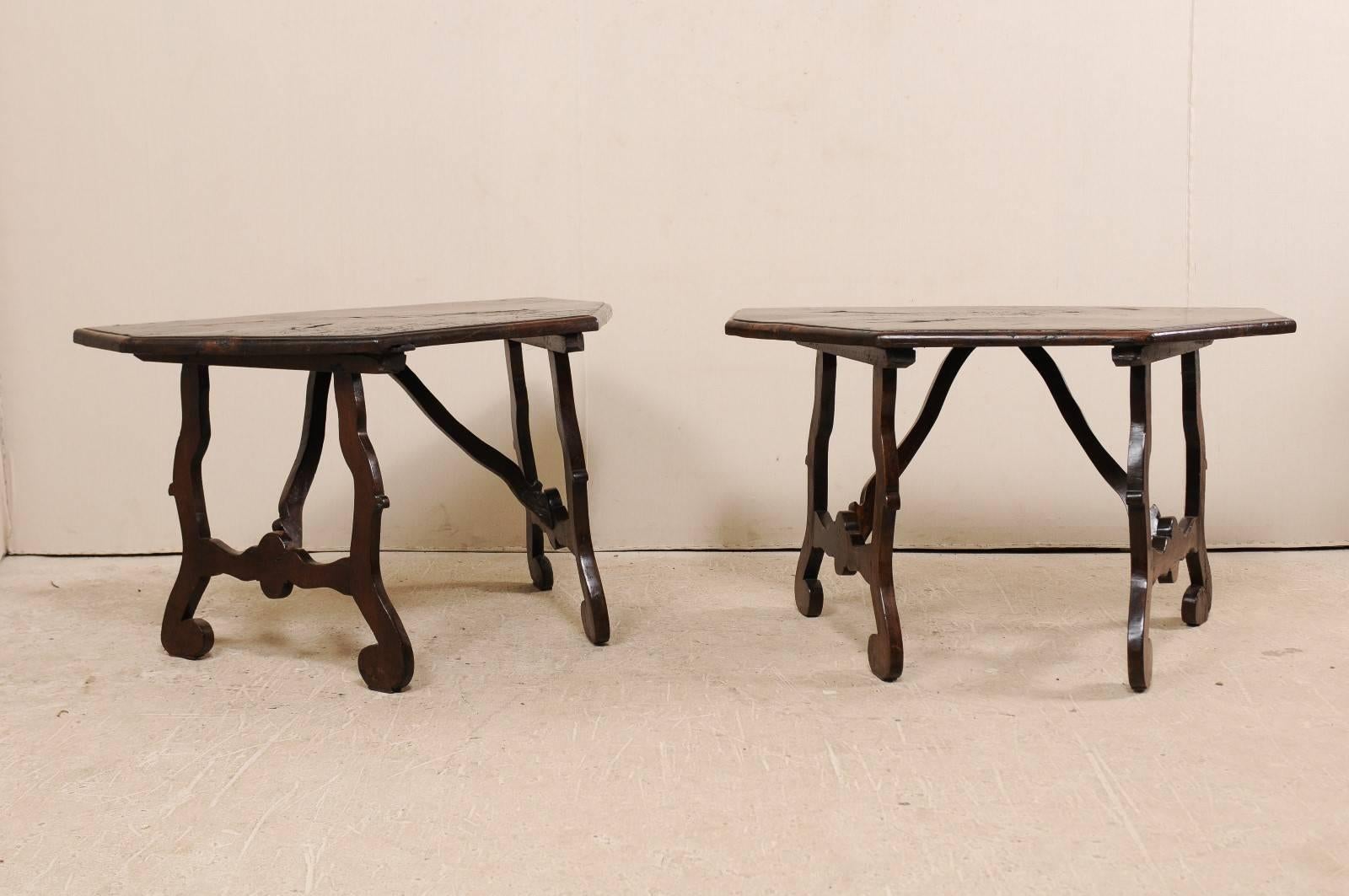 A pair of 18th century Italian demilune tables. This uniquely shaped pair of antique Italian walnut demilune tables each feature half octagon shaped tops, supported by an inwardly set trestle style base. The carved trestle supports have fluid