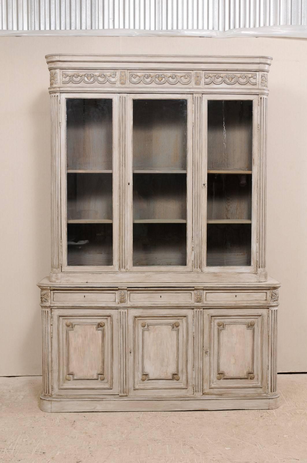 A 19th century French tall wood and glass cabinet. This tall French antique cabinet has three upper glass doors, resting on a base with three small drawers followed by three wood doors directly below. This piece features a raised cornice which is
