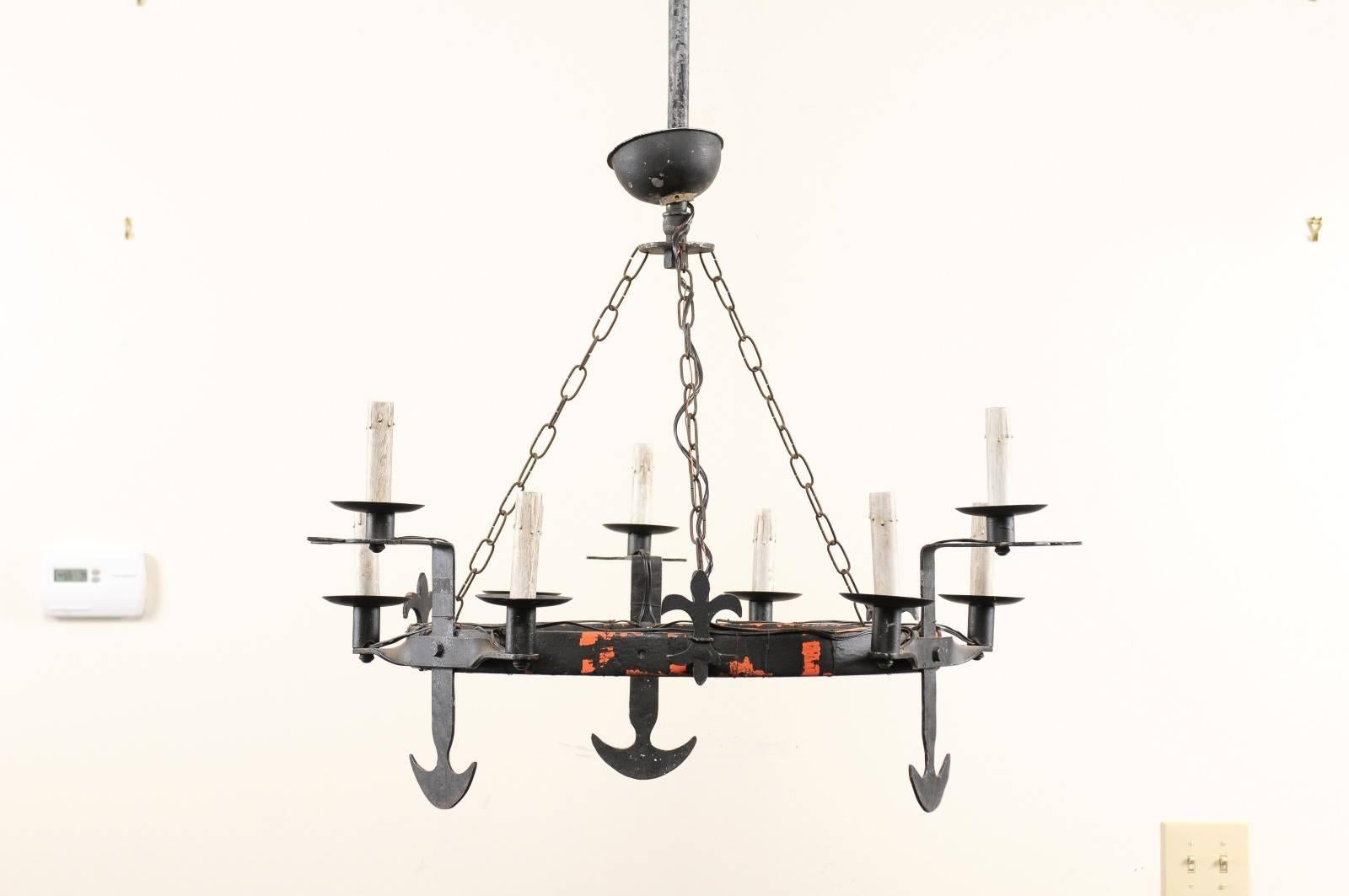 A French ring-shaped iron chandelier from the mid-20th century. This French forged iron circular-shaped chandelier features a central ring which is adorn with a fleur-di-lis motif about it's perimeter. The iron light arms have nice spade-like motifs