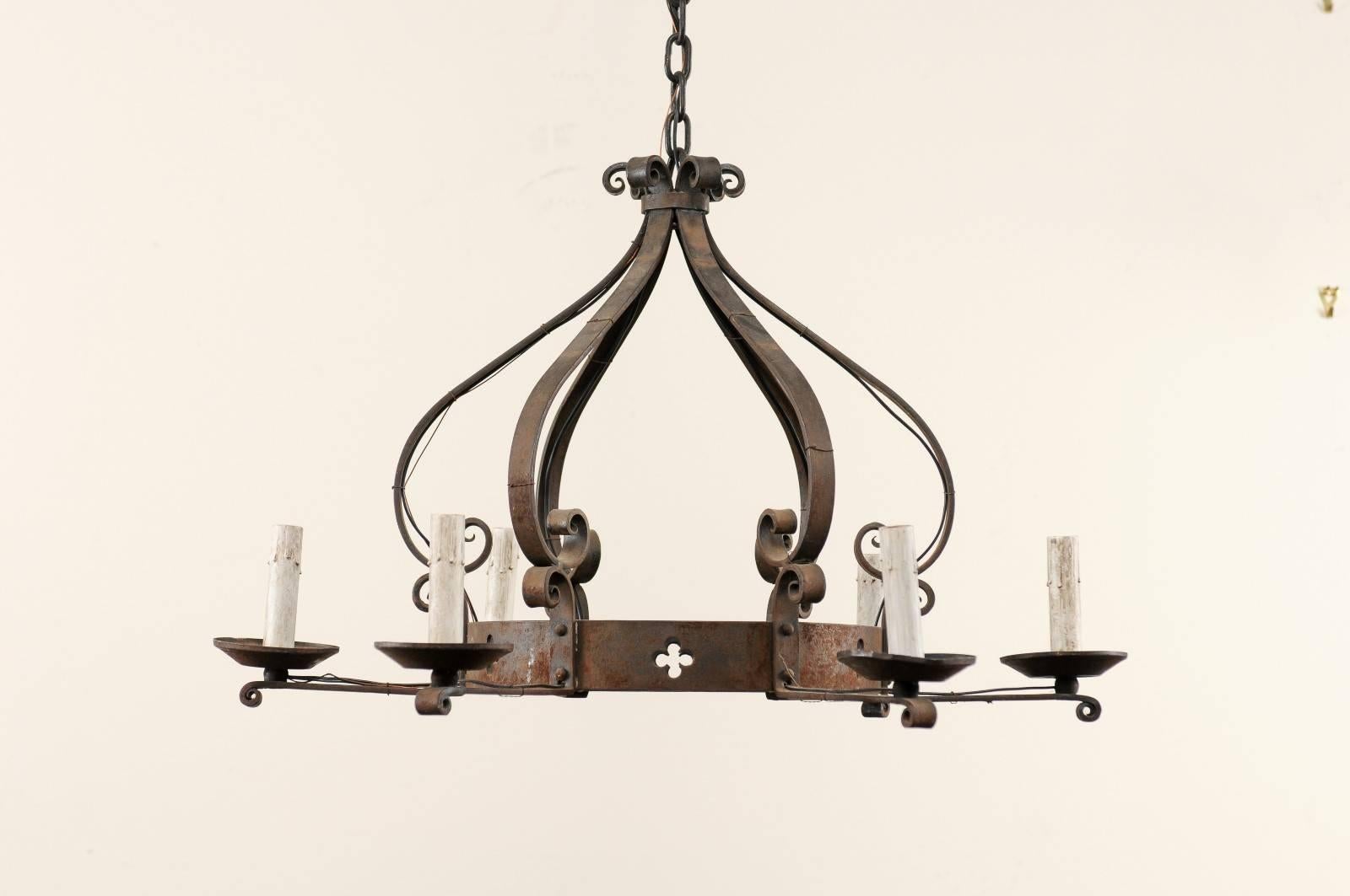 A French vintage iron chandelier with crown shape. This French forged iron chandelier from the mid 20th century features a central ring with a pierced four-leaf clover motif and six scrolling bars which raise from the ring and connect at the top,