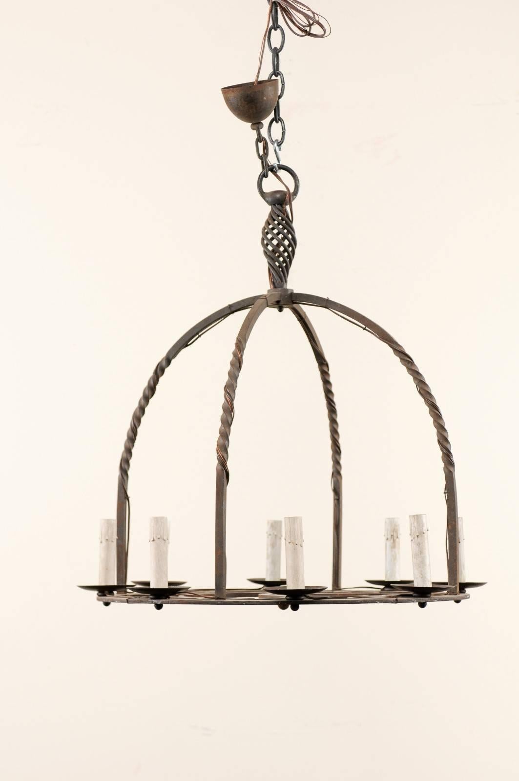 A French 19th century eight-light iron chandelier. This French forged iron chandelier features a central ring with two twisted metal pieces which criss-cross in an arching design over its base, creating a great domed-shape. The interior of the ring