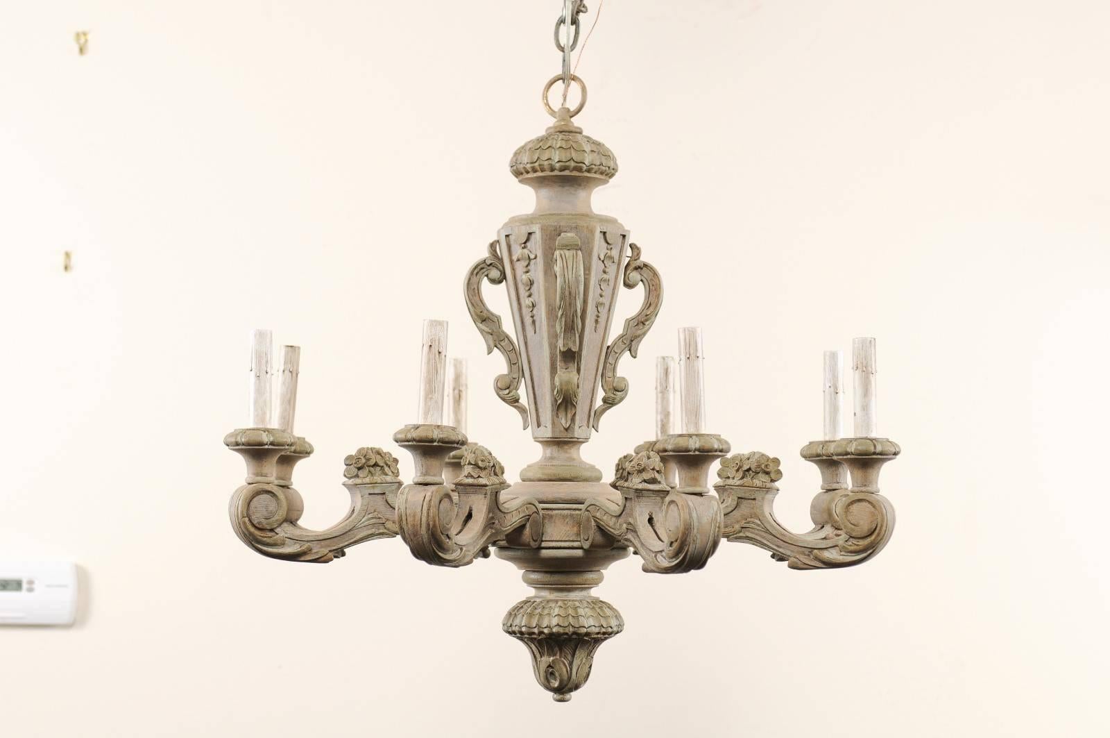 A French carved and painted wood eight light chandelier. This French midcentury chandelier features a beautifully carved column with eight scrolled arms extending outward. There is a lovely leaf and floral motif throughout, wooden bobeche and custom