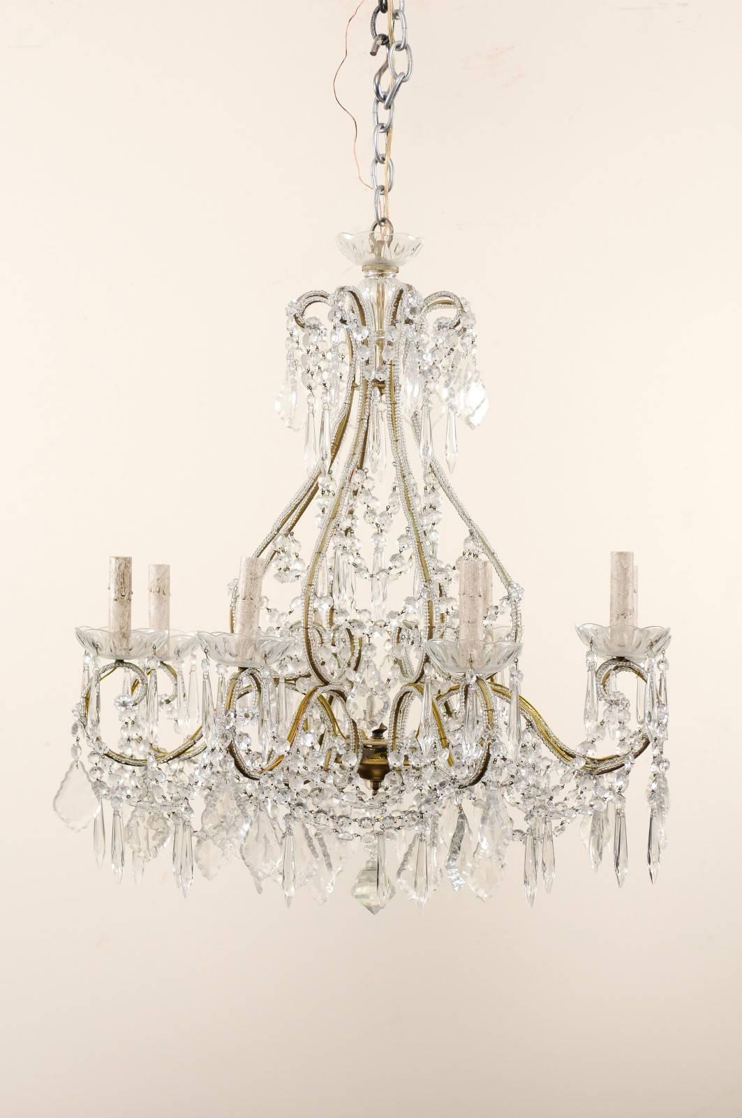 A French midcentury crystal chandelier. This French chandelier from the mid-20th century features delicately scrolled body adorn with various crystals. The armature of gilded iron is ornate with glass beading along it's structure. There is a