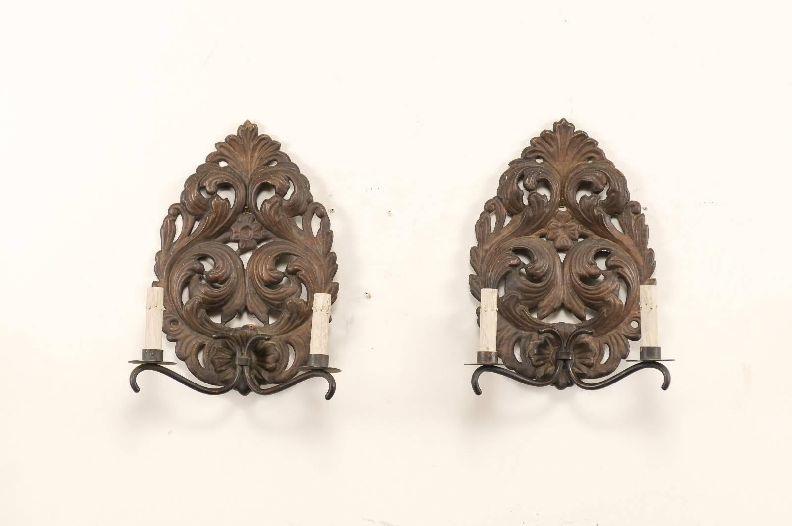 A pair of Italian two-light unwired sconces from the mid-20th century. This pair of Italian sconces each feature tole, raindrop-shaped backplates which are ornately decorated in a scrolling acanthus leaf motif. There are two gently curved metal arms