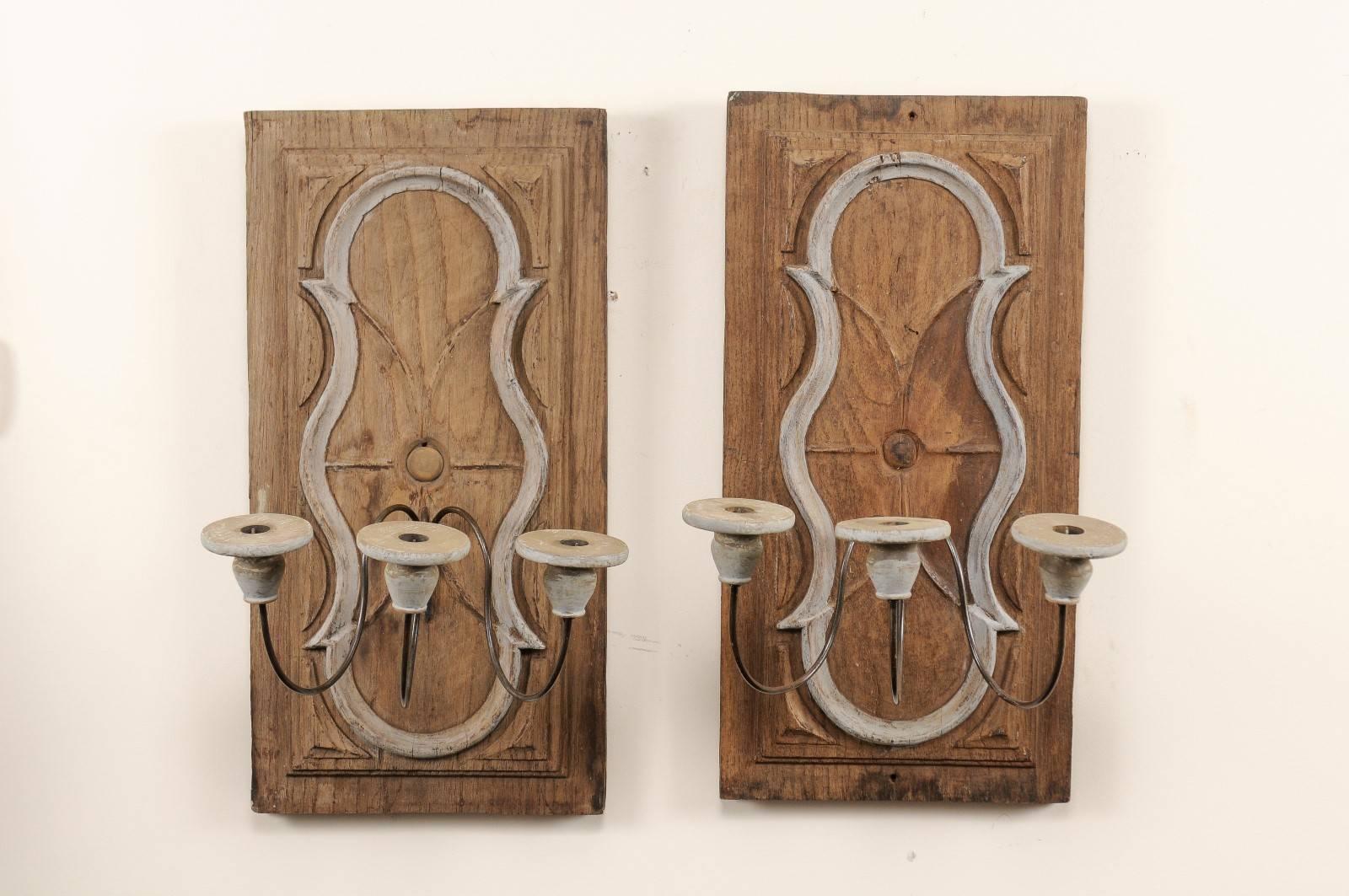 A pair of Italian 19th century carved wooden plaque sconces. This pair of Italian candle sconces have been fashioned from 19th carved wood wall plaques with 20th century arms. The carved wood back plates are vertical rectangular-shapes with fluid