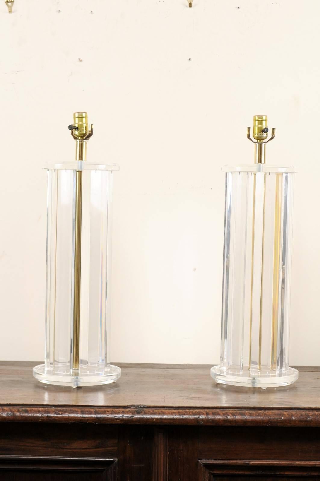 A pair of American Lucite table lamps from the mid-20th century. This pair of midcentury lamps have a round-shaped body, comprised of Lucite posts mounted in a circle between a circular upper cap and wider, circular base, also in Lucite. There is a