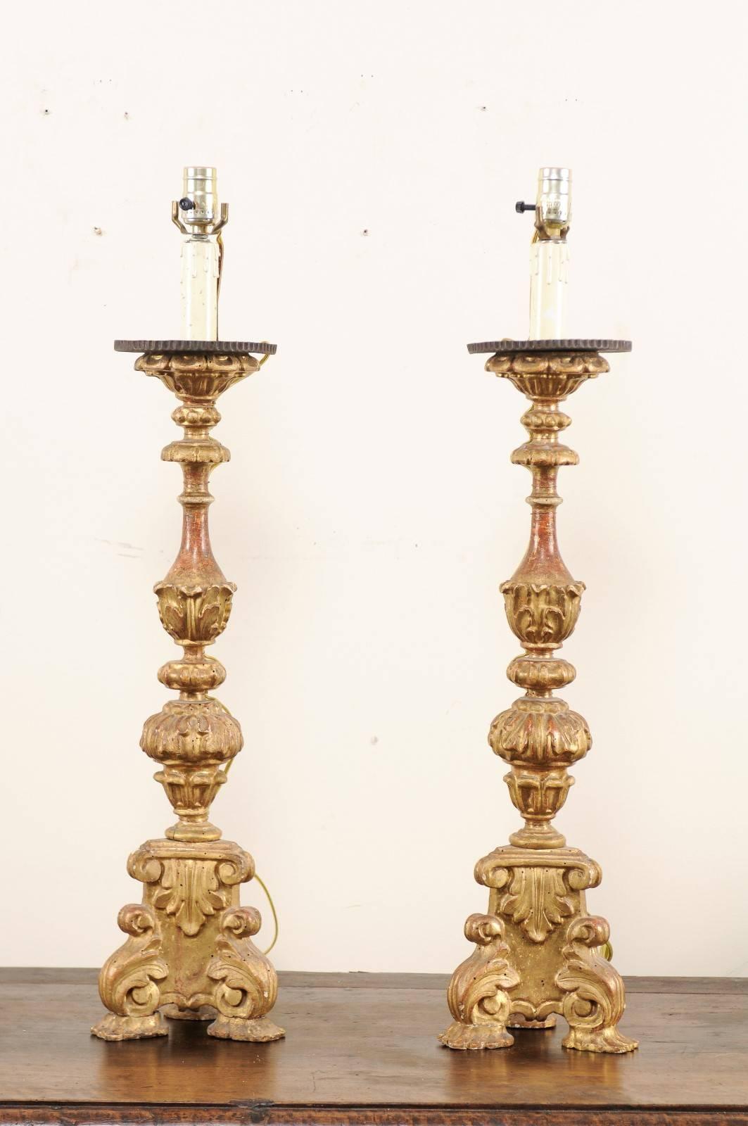 A pair of 19th century Italian gilded candlestick lamps. This pair of Italian 19th century (or possibly earlier) candlesticks, decorated in leaf and scroll motif carvings throughout, have been fashioned into table lamps. These Italian gilded lamps