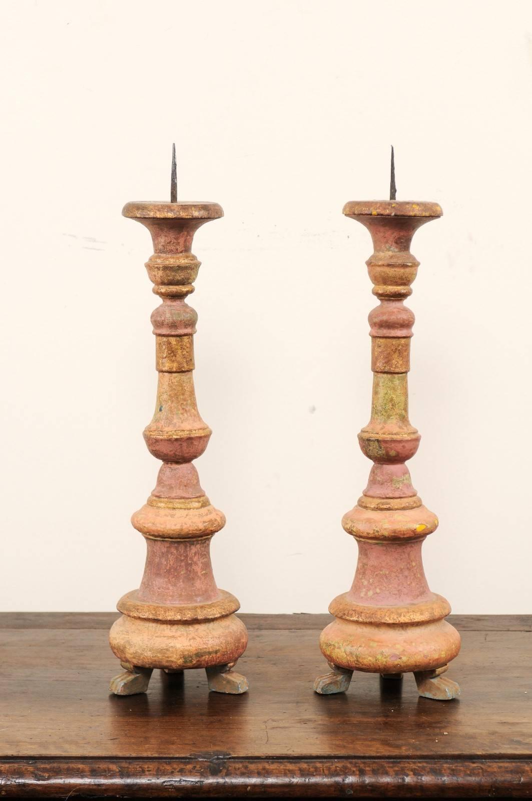 A pair of Portuguese 19th century wooden candlesticks. These antique candlesticks are from the former Portuguese enclave of Goa in India. They have carved, rounded bodies and are raised up on three feet, which project outward from the candlestick