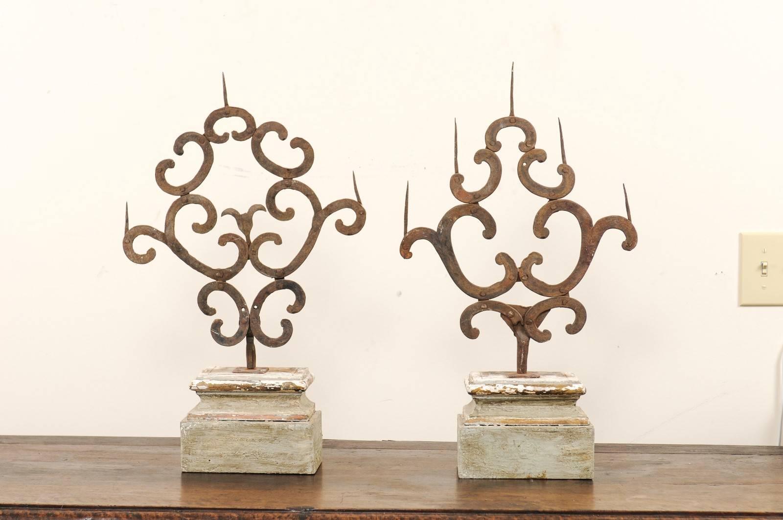 A pair of 18th century, Italian prickets. This pair of antique Italian prickets of hand-forged iron feature a beautiful succession of decorative c-shapes, giving life to their overall botanical shape, which rises up from a singular stem. These