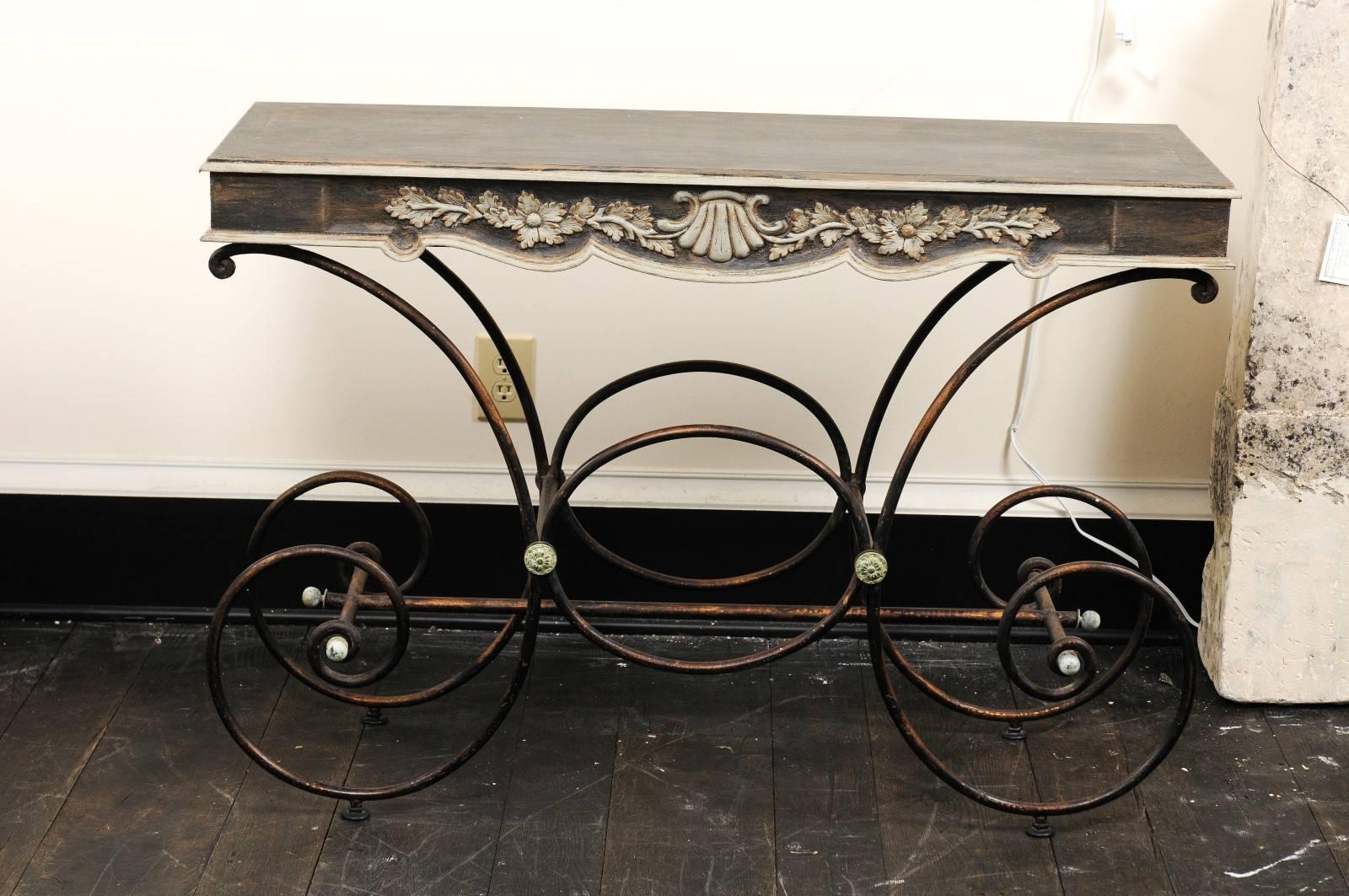 Une table de boulangerie française vintage avec un plateau en bois peint et une base en fer. Cette table française fantaisiste présente un plateau en bois peint, avec des motifs floraux et de coquillages festonnés et sculptés sur le centre avant de