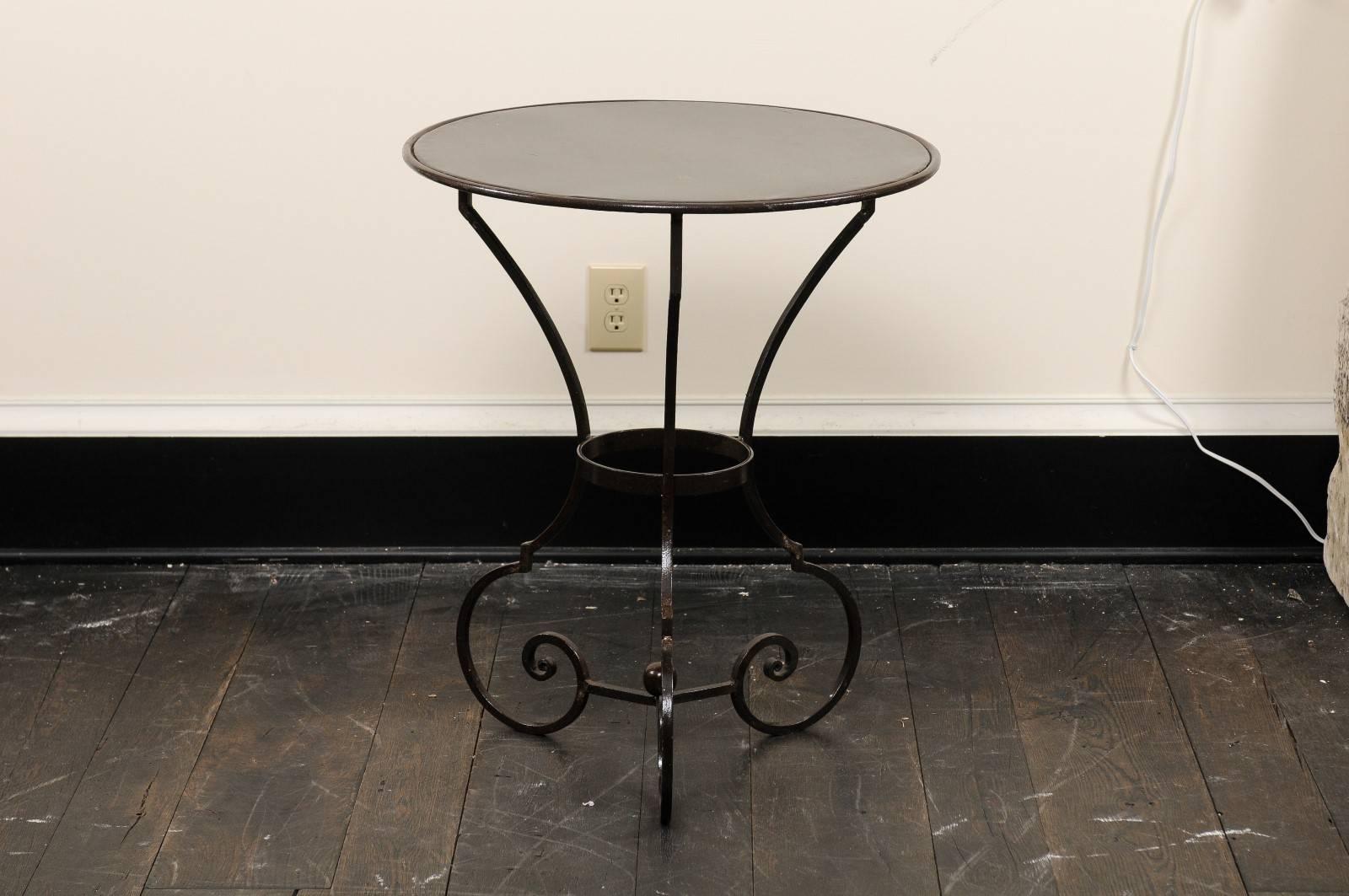 A pair of petite-sized bistro tables. This pair of round guéridon tables have been custom-made and feature round metal tops, two feet in diameter, raised upon a steel base comprised of three fluid legs, which turn inwardly at their bottoms,