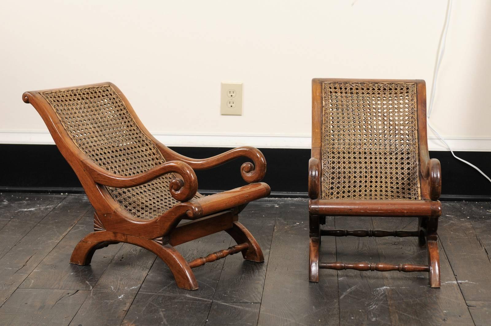 Pair of 19th century English children's chairs. This pair of antique English chairs feature cane seat and backs with curvy teak wood frames. The carved teak arms curl into scrolled knuckles. The legs are designed of two c-shaped pieces, supported by