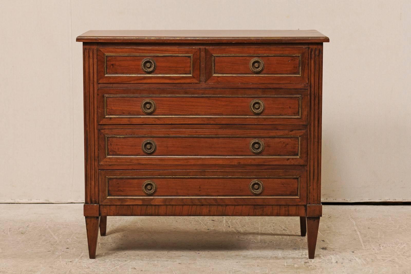 A vintage French wood five-drawer dresser. This antique French dresser features two half drawers over three longer drawers. Each drawer has beautiful metal trimming and are adorn with a wreathed ring pull, with a single flower at their centers.