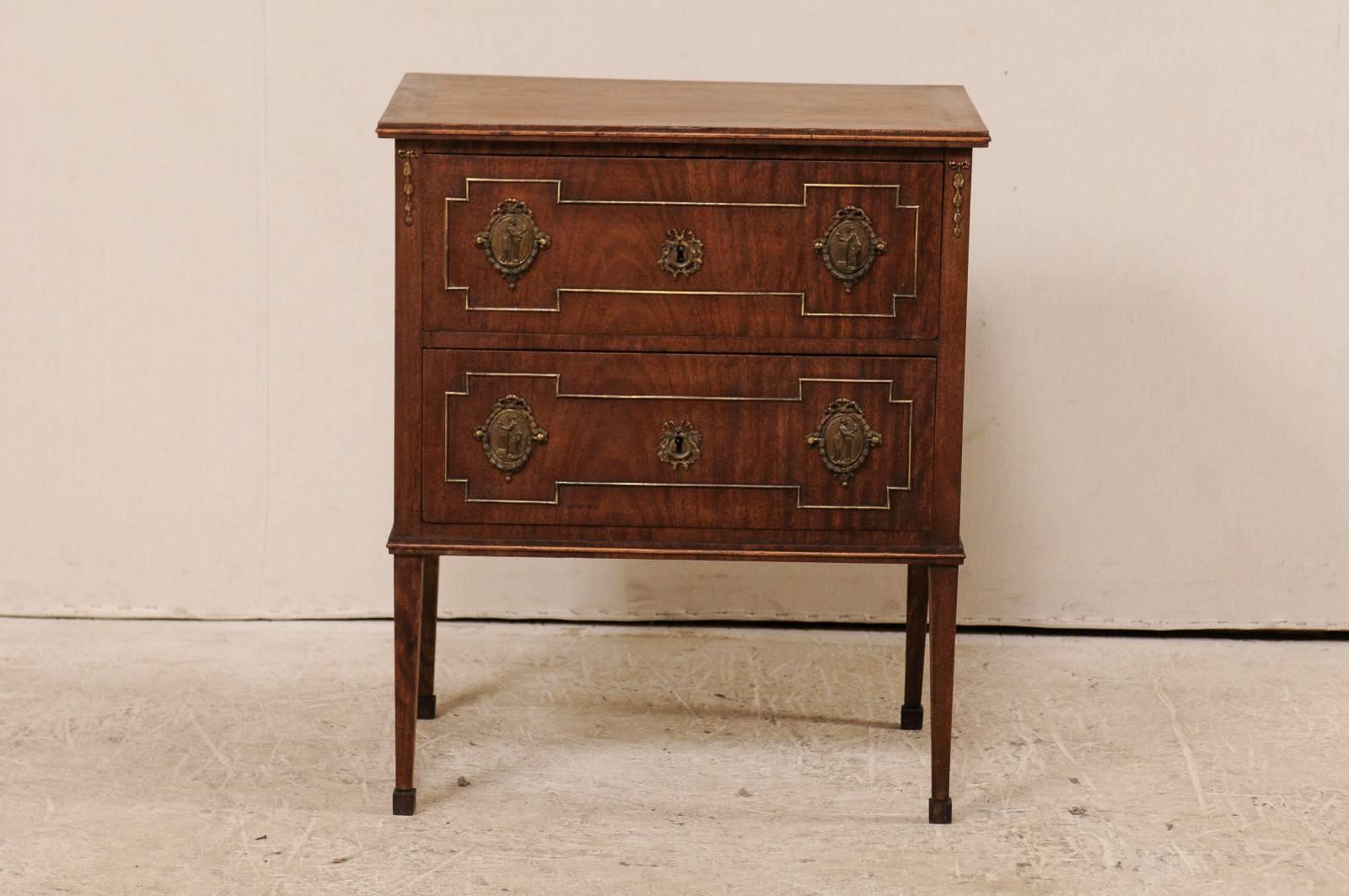 A French mahogany two-drawer chest from the early 20th century. This antique French chest features two dovetailed drawers decorated with exquisite Empire style hardware. The keyholes are hidden behind the ornamental escutcheons in their center. This