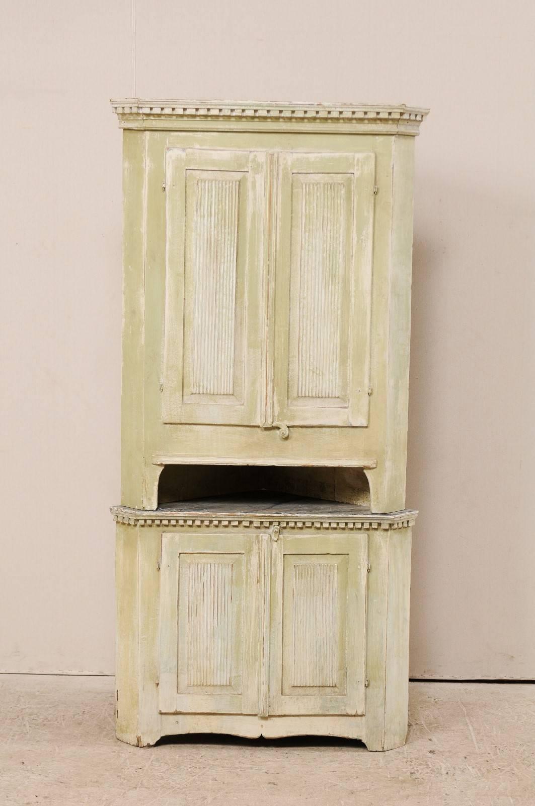 A Swedish late 18th century period Gustavian painted wood corner cabinet. This Swedish Gustavian corner cabinet features reeded doors, dentil molding just below the upper cornice and mid section, and a scalloped accolade style carved skirt. This