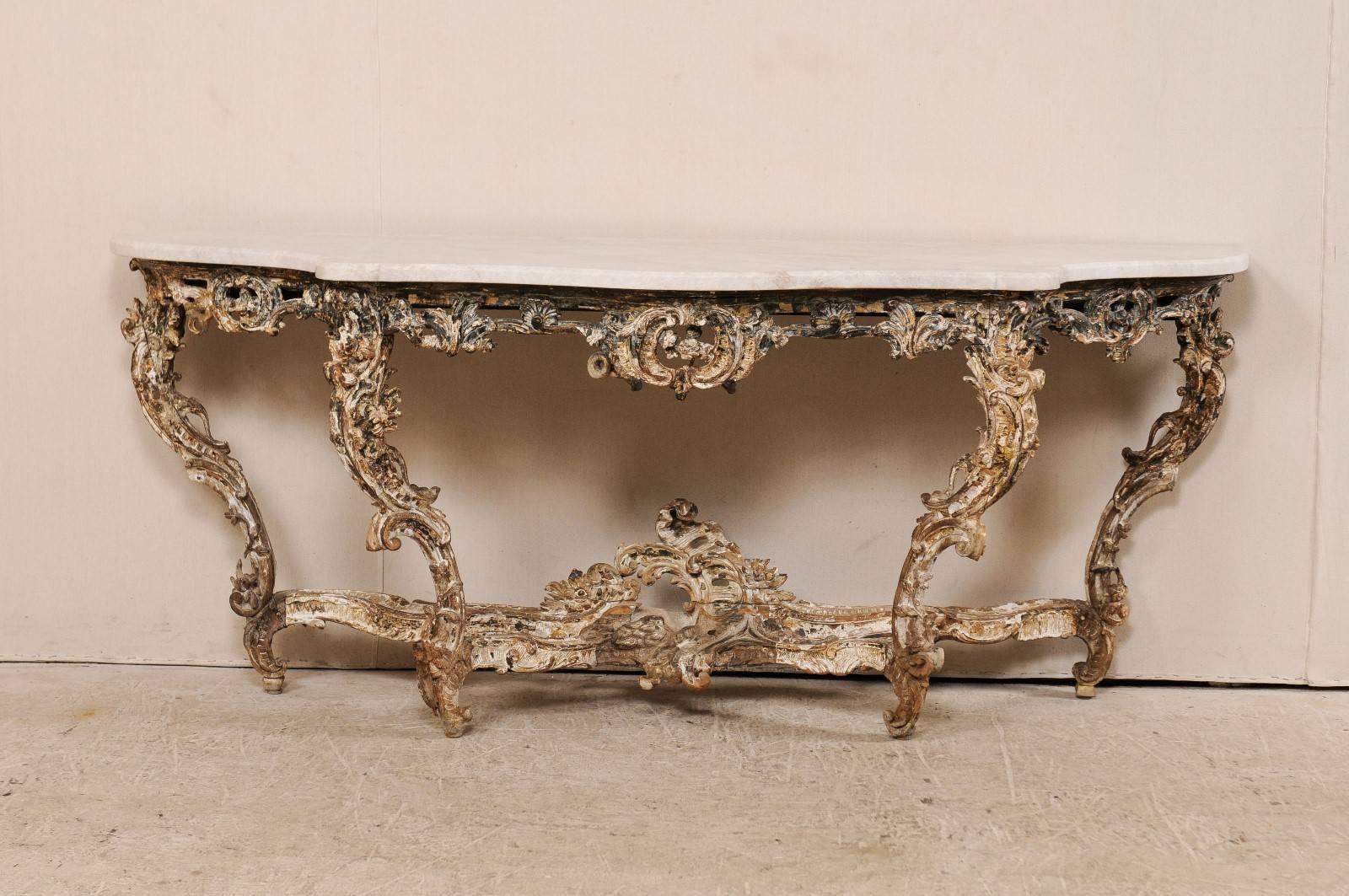 A French carved wood Rococo console table with marble top, 18th century. This gorgeous French console table features the typical French elaborate carvings of the Rococo period along the skirt, cross stretcher and four legs. The base is gesso and
