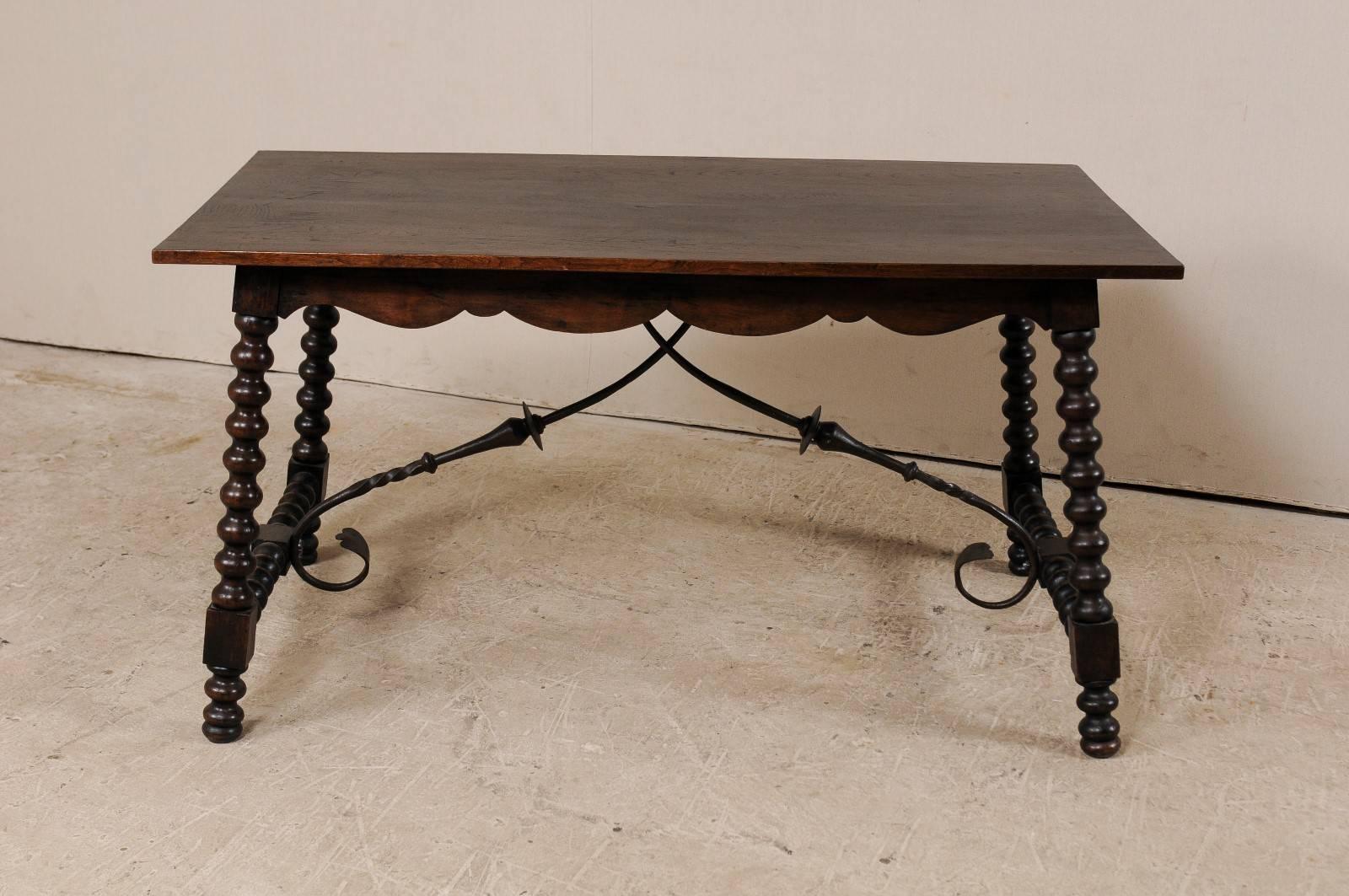 A Spanish 19th century wood an iron stretchered table. This antique Spanish table features a rectangular-shaped top which rests above it's beautifully scalloped apron. This table has outwardly tilting bobbin carved legs, which are supported with