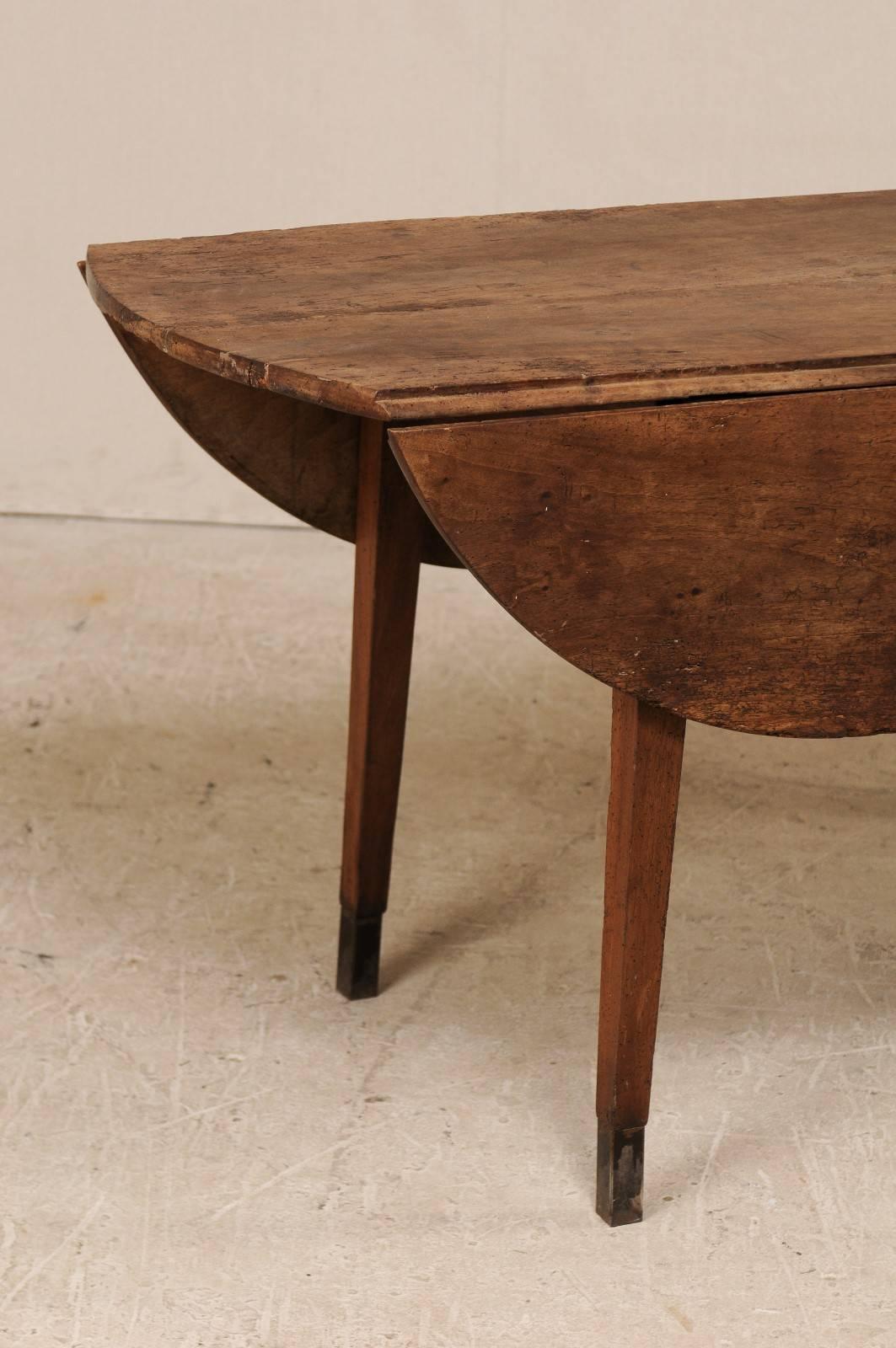 A French early 19th century drop-leaf table. This French table has dual drop-leaf sides that open into an oval shape. This 19th century table has clean, simple lines. It sits upon four squared and gently tapered legs, which each terminate into