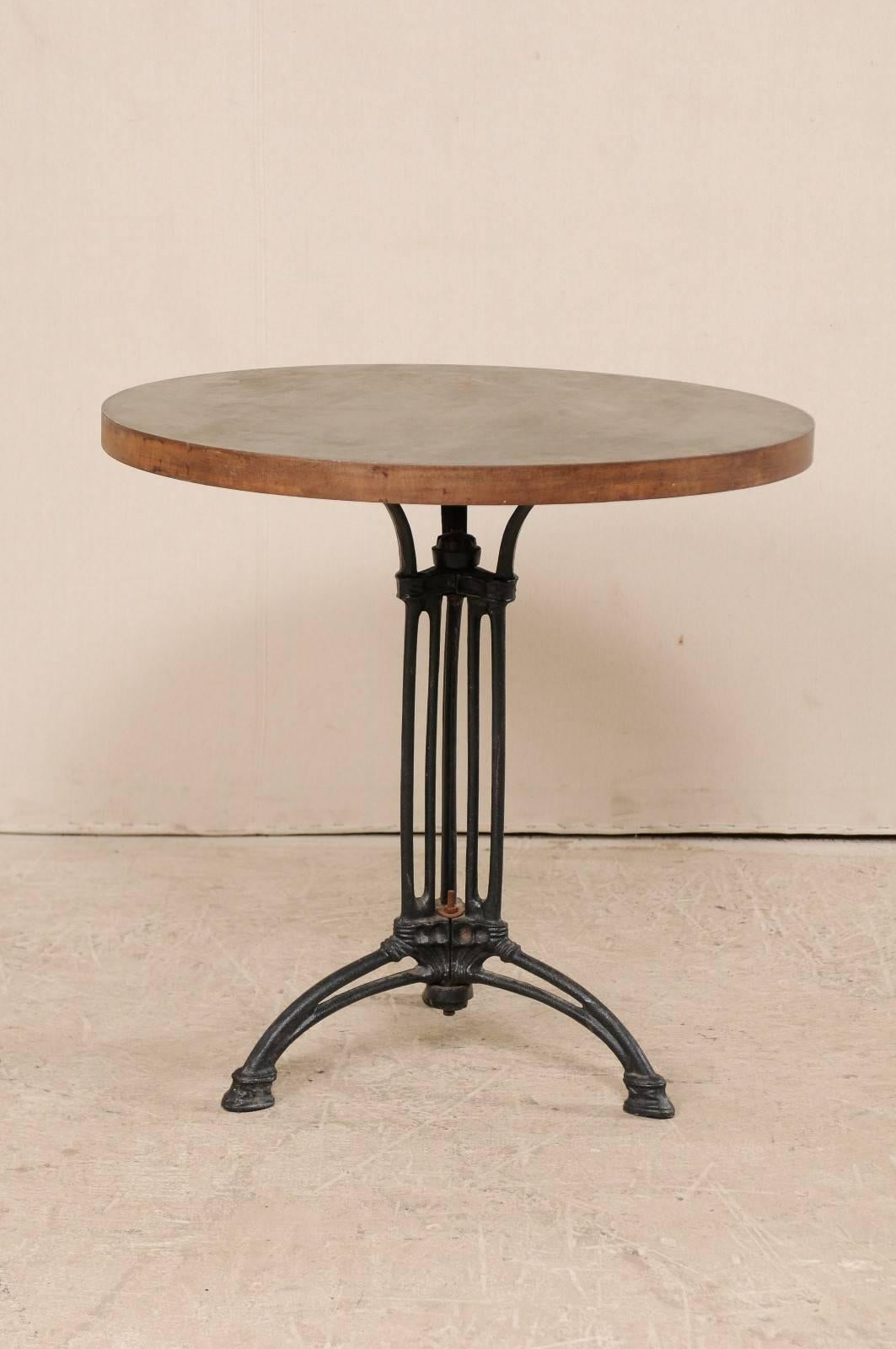 A French iron bistro table. This French bistro table consists of a early 20th century iron base with a contemporary top. This Industrial style bistro table is round-shaped and features a central black iron centered column base with tri-pod feet and