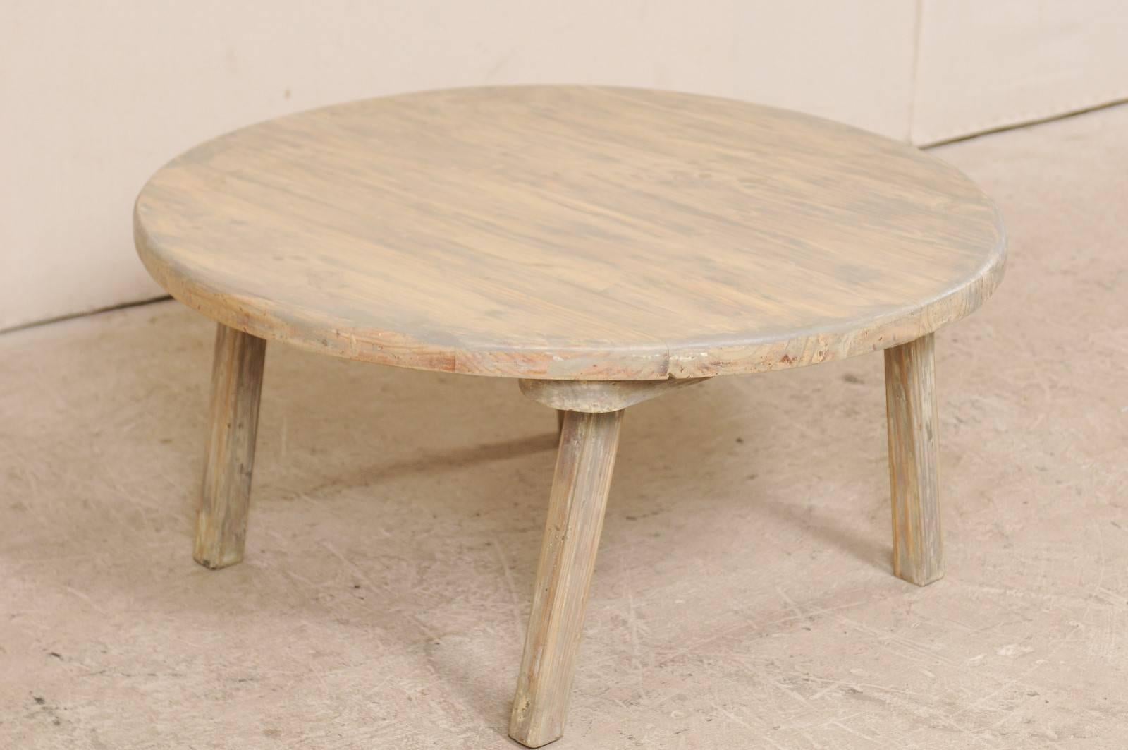 A vintage American painted wood coffee table. This American coffee table features a round-shaped top which is raised by four squared legs. This rustic little table has a wash of grey and cream, with much of the wood grain showing through. This