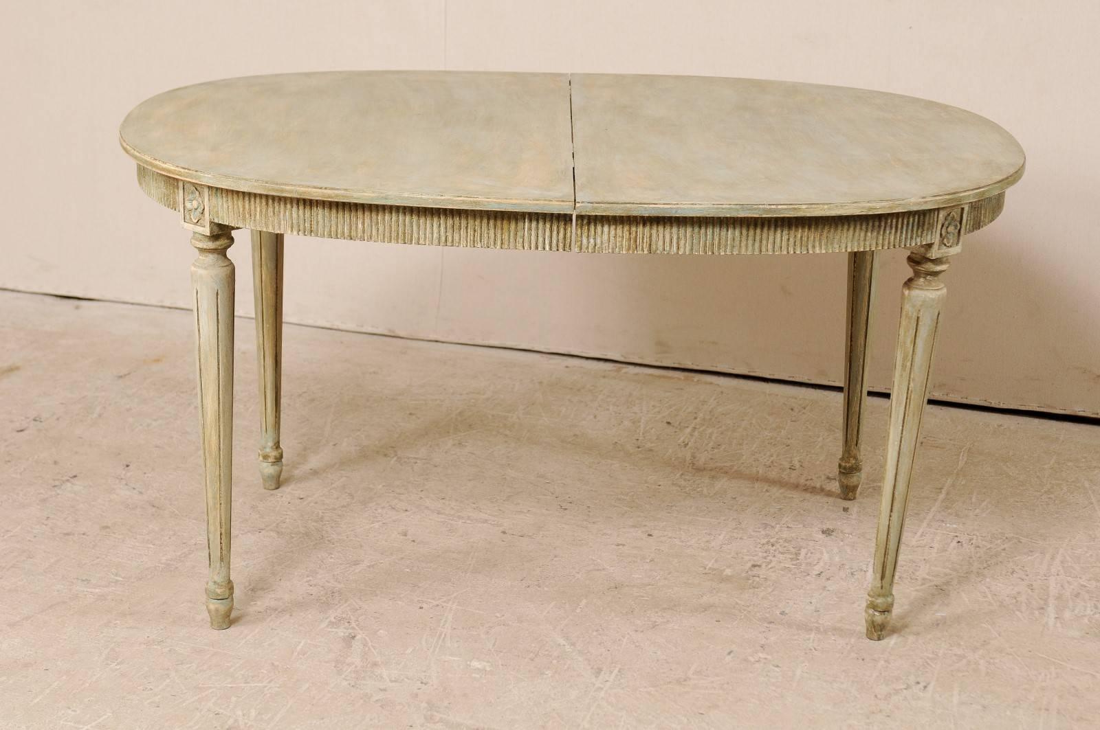 A vintage Swedish Gustavian Style painted wood table. This Swedish table features an oval-shaped top, and a reeded apron with carved rosette accent pieces above which are above each of its four rounds, fluted and gently tapered legs. The coloring is
