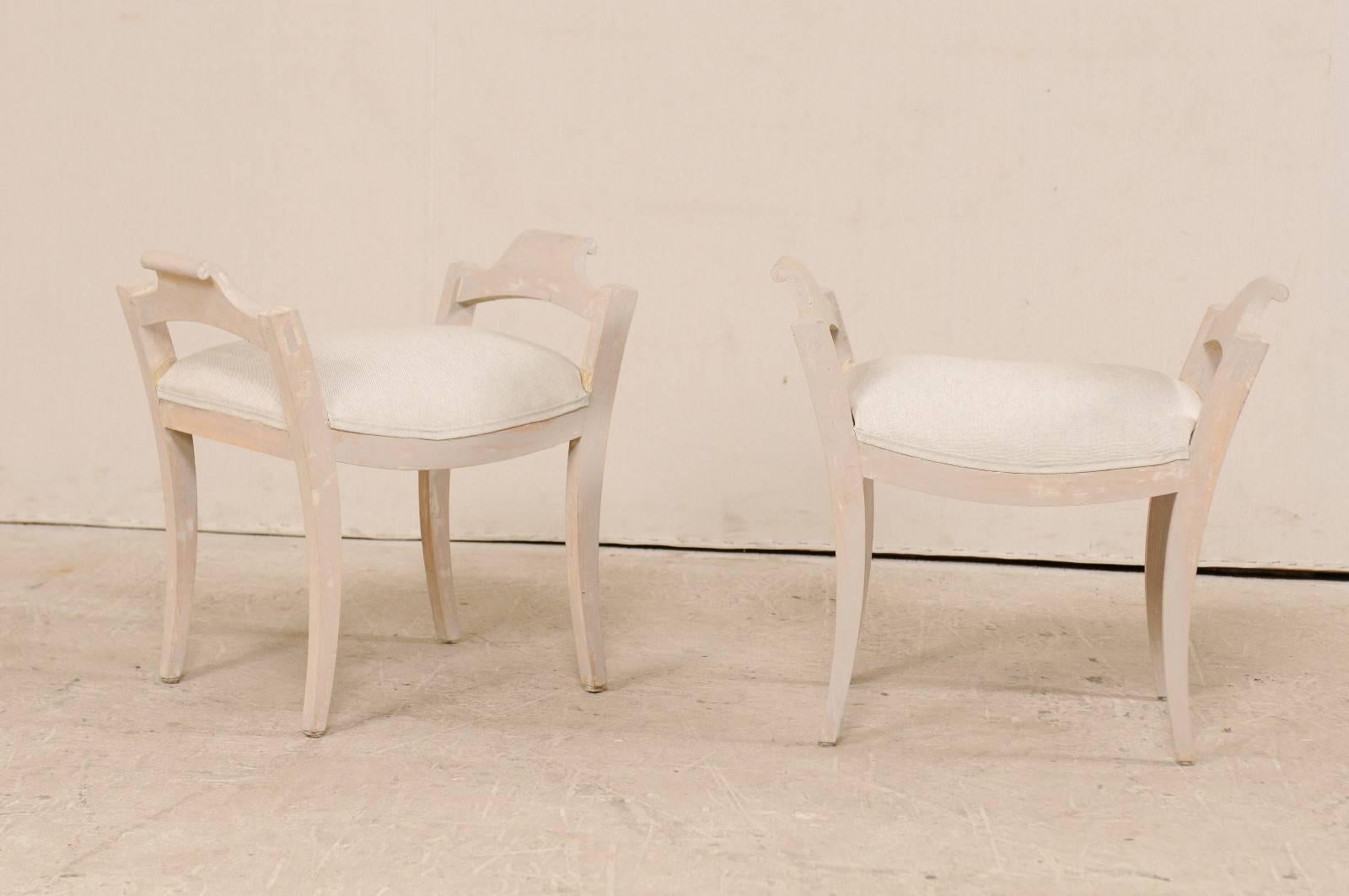 A pair of Swedish 19th century stools. This antique pair of petite wooden benches (or footstools) feature nice clean lines, gently curved and tapered legs, and raised side. These stools have a wash of pale grey, and the attached seats have been