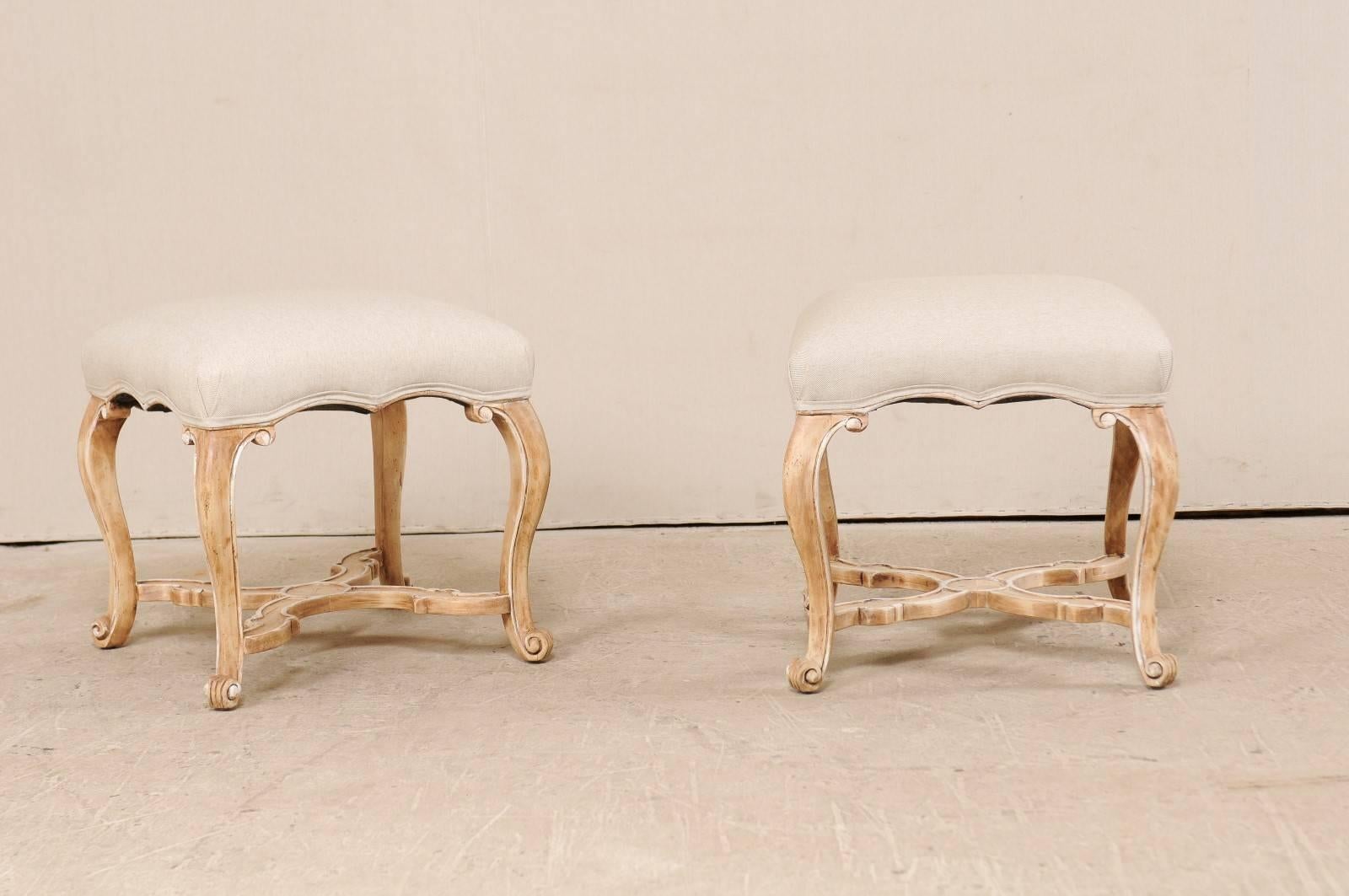 A pair of carved wood and upholstered stools by Los Angeles based manufacturer, Minton-Spidell. These wonderful pair of stools feature four nicely carved cabriole legs, supported with a curvy X-stretcher with raised edges and circle ornament at