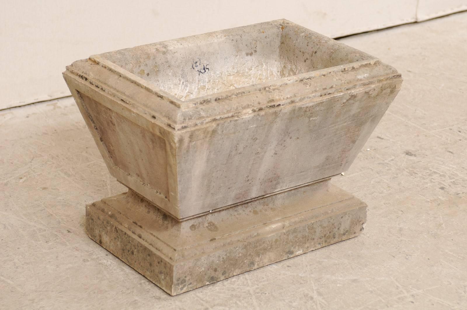 A European stone planter from the early 20th century. This antique, hand-carved stone planter has an overall rectangular-shape, with recessed panel designed sides, which tapers slightly towards the bottom. Just below the main body, the stone is
