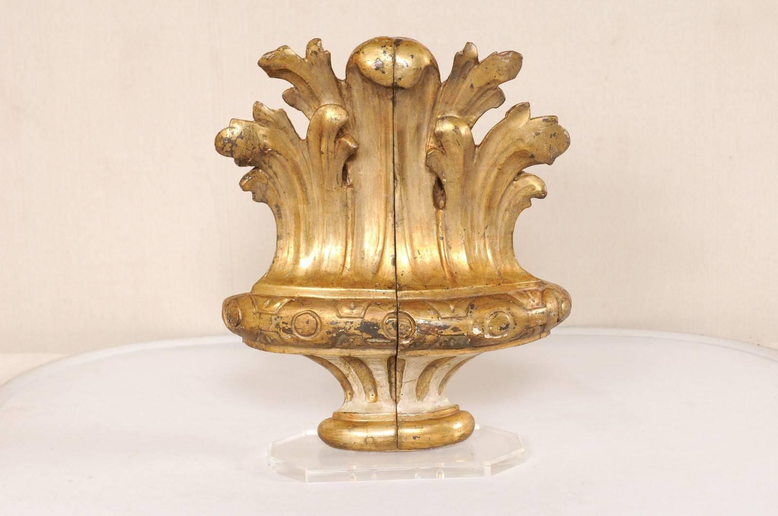 An early 19th century Italian carved wood gilded fragment on custom base. This Italian hand-carved fragment features an urn shaped body, decorated in circular patterns and fluting details, with acanthus leafs raising from its top. This fragment has