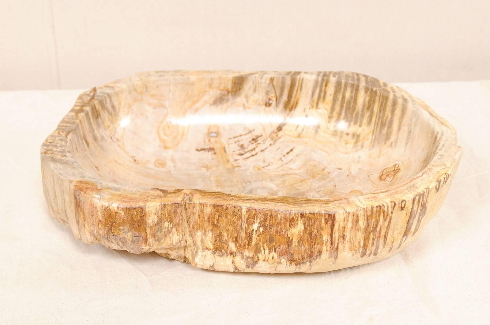 A beautiful petrified wood sink. This petrified wood sink has a mostly oval shape with a flatter back-side. The colors are primarily beige and cream, with warmer brown and rust tones. While the interior of the bowl has been polished, the surround