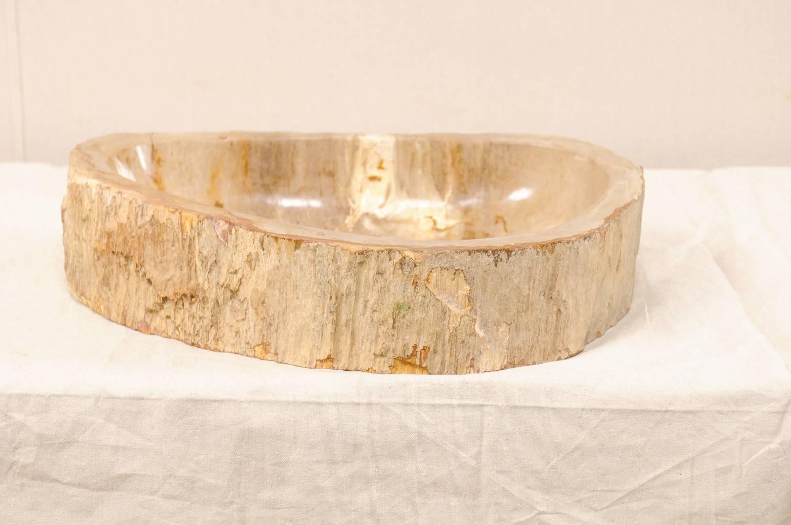 A petrified wood sink. This petrified wood sink has a shape best described as a rounded triangle with a flatter back-side. The colors are primarily in cream and beige, with warmer brown and rust tones. While the interior of the bowl has been