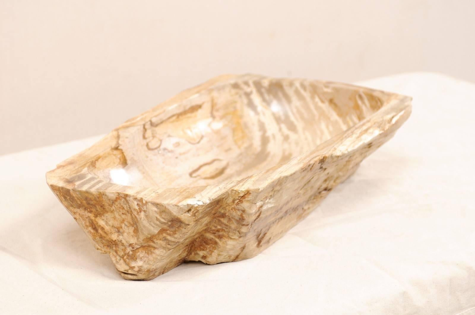 A petrified wood sink. This petrified wood sink has an oblong shape, with flatter back and right sides. The colors are primarily in beige and cream tones, with richer brown and taupe tones. While the interior of the bowl has been polished, the