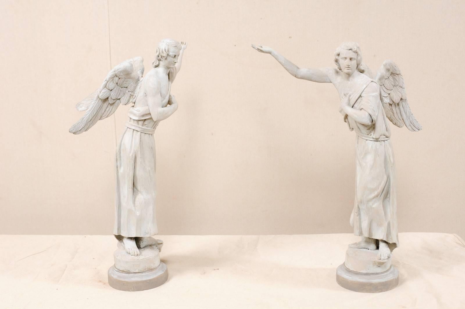 A pair of French carved wood angelic figures from the 19th century. This pair of antique figures are portrayed as an angel or winged male figure, draped loosely in a robe, with bare feet and shoulder, each having one arm reaching upwards with palm
