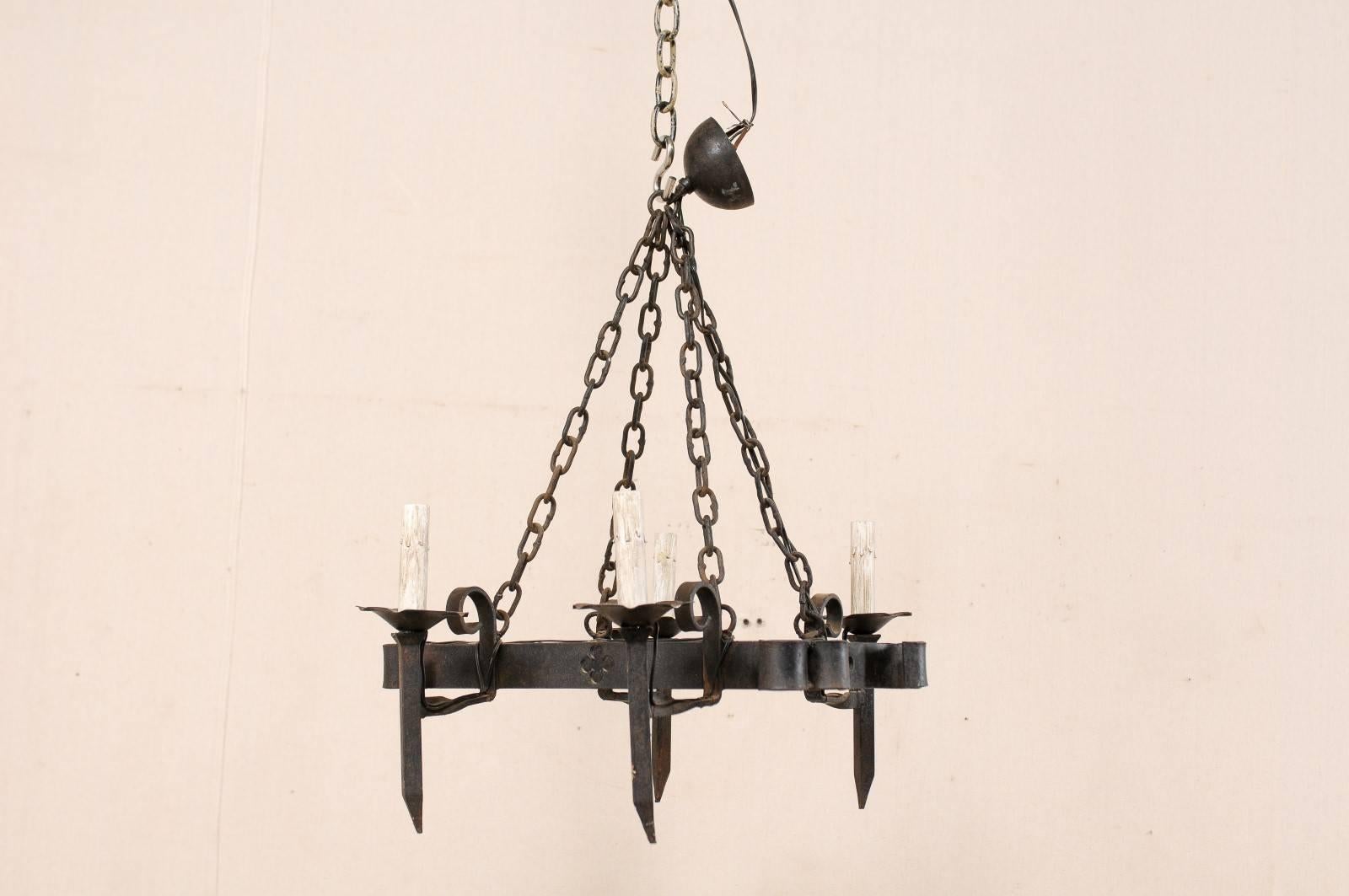 A French four-light forged iron chandelier with quatrefoil pierced motif. This mid-20th century French black iron chandelier has an open, center body adorn with pierced clovers, and two torch-light arms at opposing sides. The four torch lights