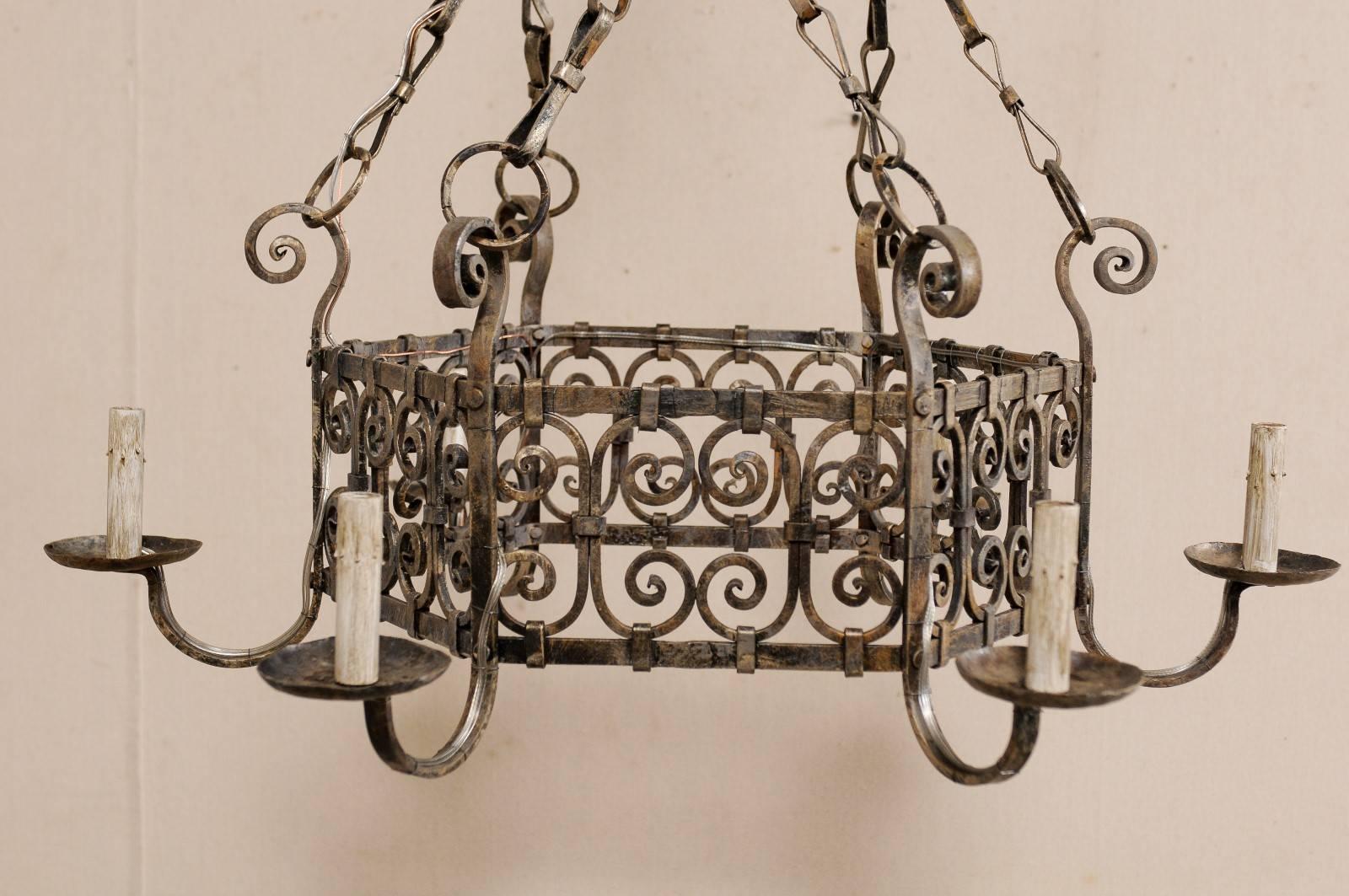 A French mid-century six-light iron chandelier. This lovely French chandelier from the mid-20th century has a rounded hexagon shaped central ring which is adorn in a series of connected scrolled designs. The six arms are attached around the
