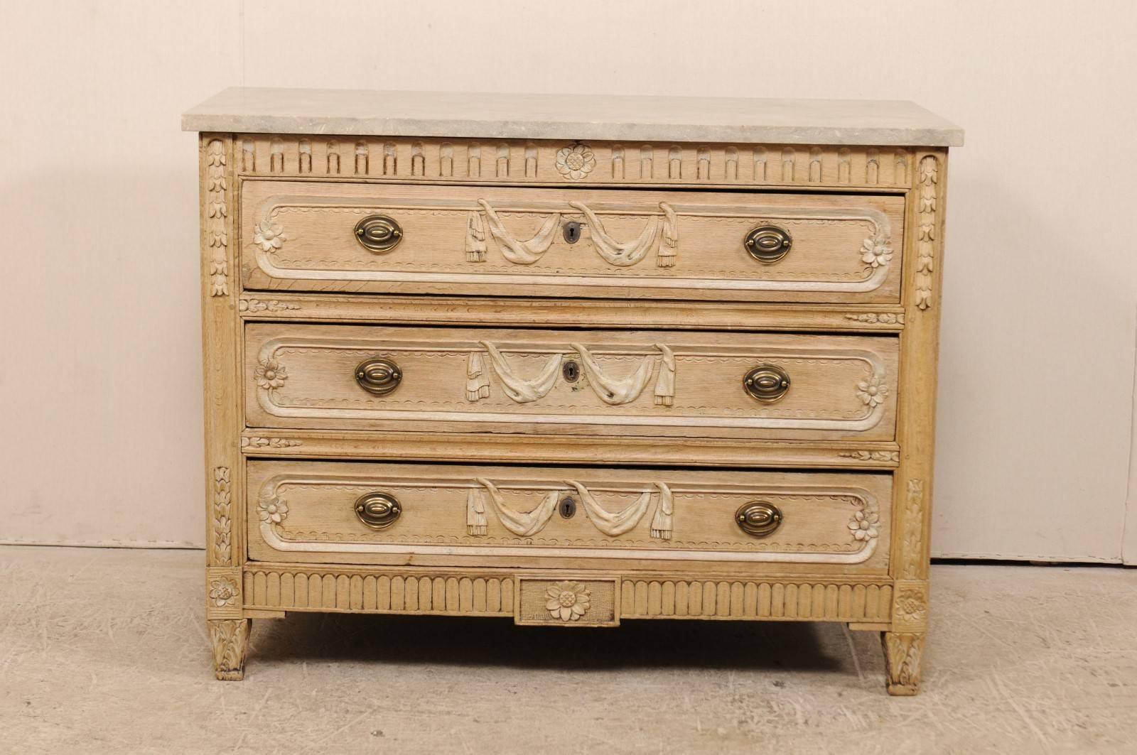 A French, early 19th century carved wood chest with a fossilized and honed marble top. This antique oakwood chest of three drawers features beautifully carved motifs of swagged ribbons falling gently about the center of the drawer fronts, just over