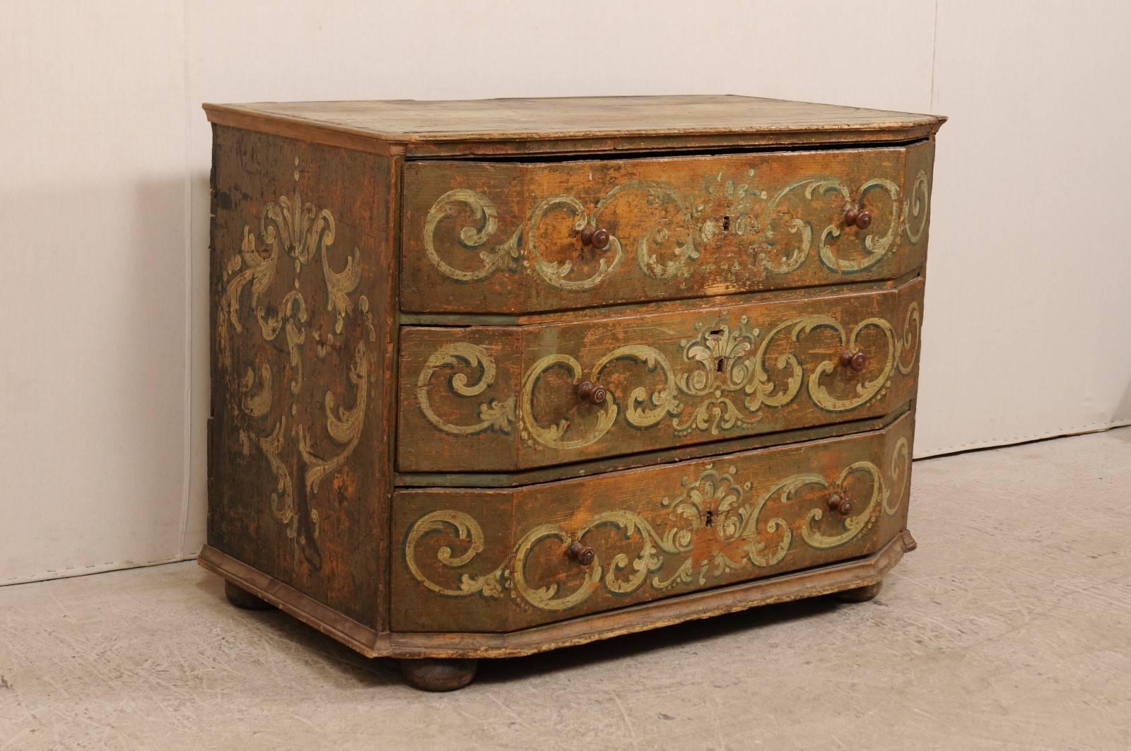 An 18th century Italian commode with canted drawers and hand-painted details. This antique Italian three-drawer commode has been uniquely designed with large canted drawers, and top which mimics this shape, giving this piece an robust chest. There