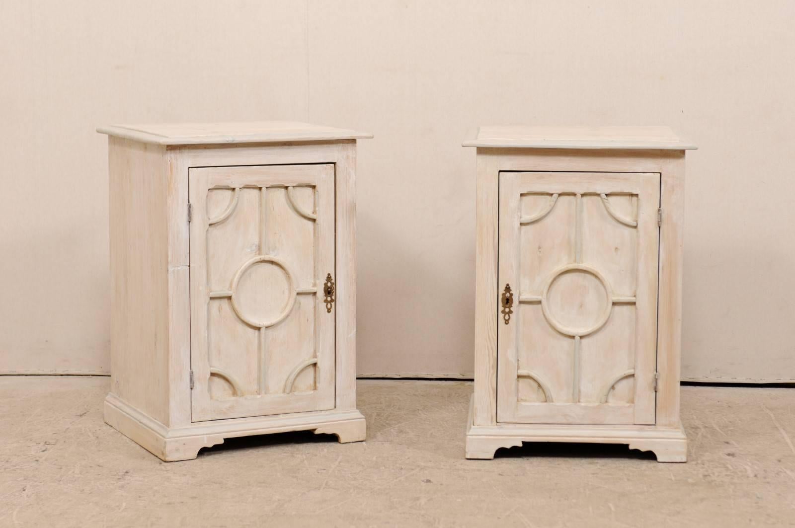 A pair of English painted wood side chests or tables from the mid-20th century. This pair of midcentury side cabinets features a recessed panel single door which has raised geometrically designed trim details, emphasized with a circle at their