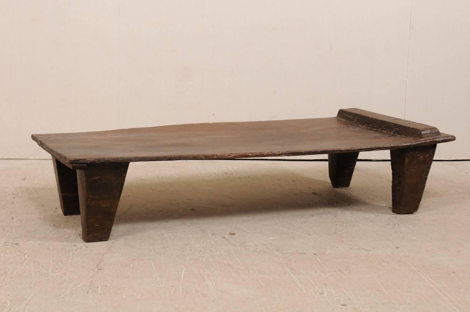 A primitive wood Naga coffee table from the early 20th century. This antique piece originated as a wood bed from the Naga tribes of Nagaland, North East India. It has been carved out of a single log, is raised on four widely carved feet and has a