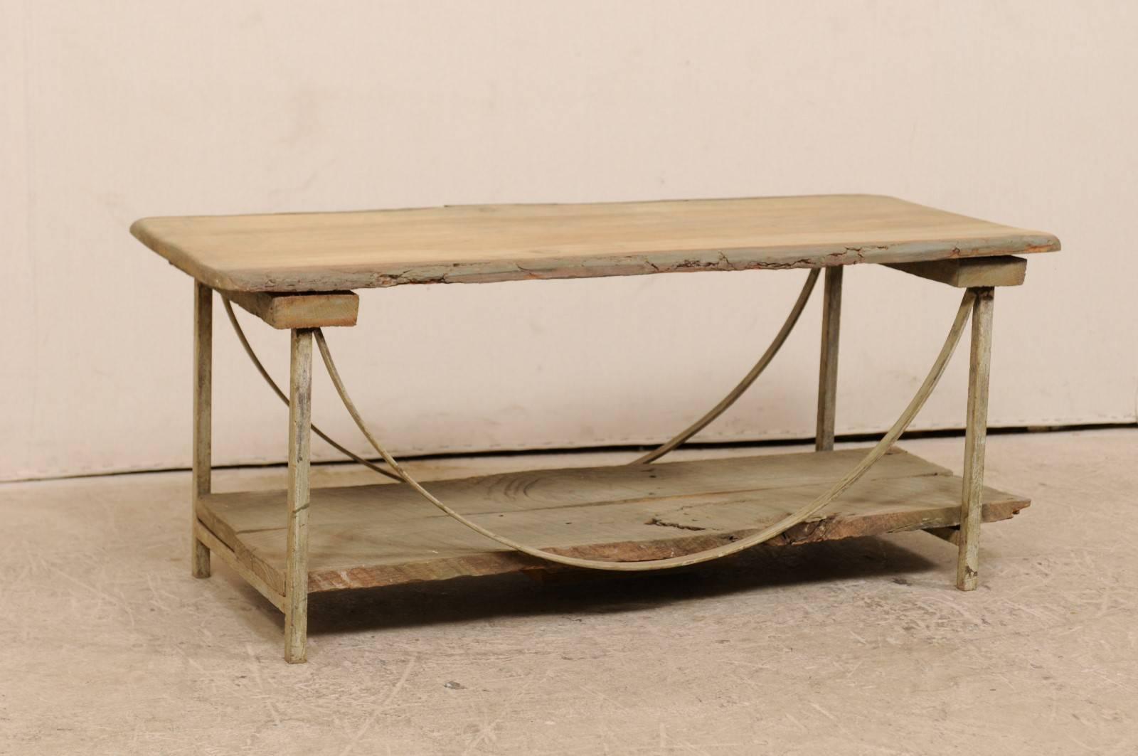 A vintage American wood and iron two-tier coffee table. This vintage coffee table features a live-edge sycamore wood slab top which is held within a painted iron base of four straight legs and beautifully swagged side stretchers along each of it's