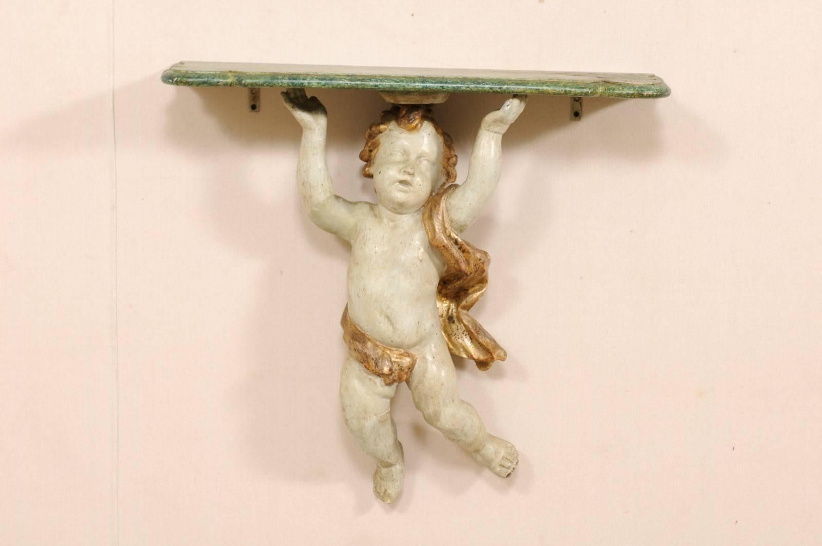 An Italian late 18th-early 19th century smaller-sized carved putto wall-mounted console table. This antique Italian wall-mounted console shelf features a three-dimensional carved wood and gesso putto, with gold gilt details throughout it's hair and