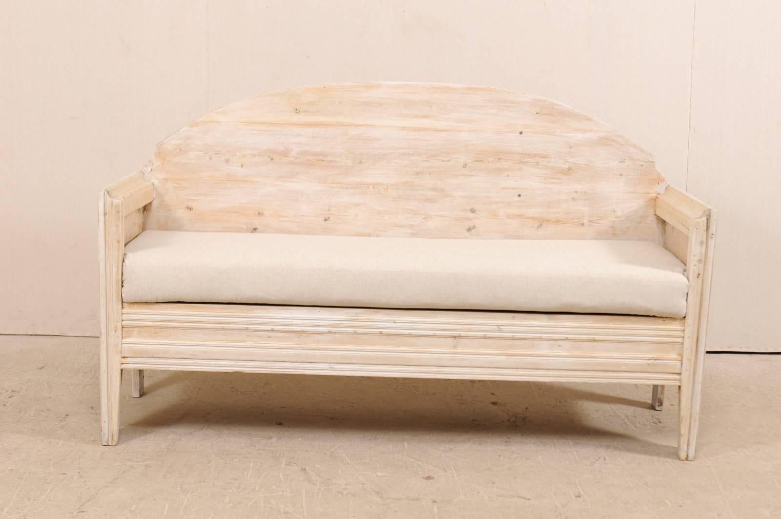 A Swedish sofa bench from the early 19th century. This antique Swedish wood sofa bench features a nicely arched back with decorative cut-out at each far corner, high arms, and clean linear lines across the front skirt . This bench is raised on