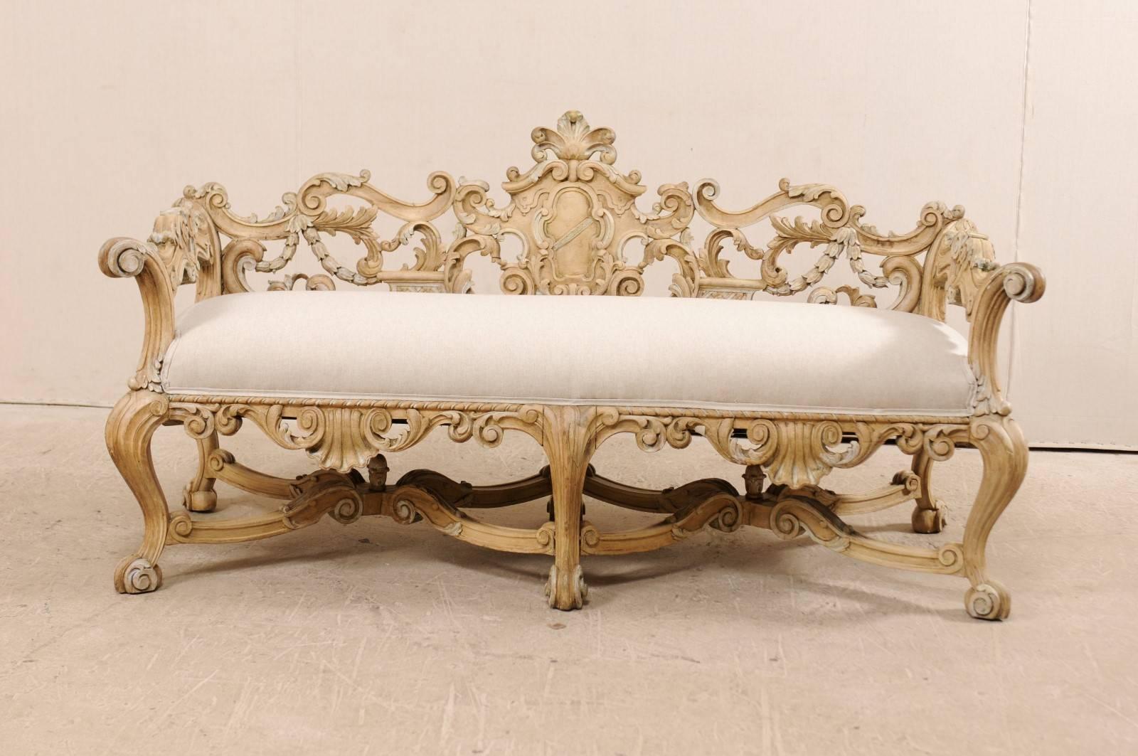 An exquisite, richly carved Italian wooden bench from the 19th century with upholstered seat. This antique Italian Baroque style bench, circa 1880, features elaborate carvings throughout it's back and skirt in a shell, acanthus leaf, and floral