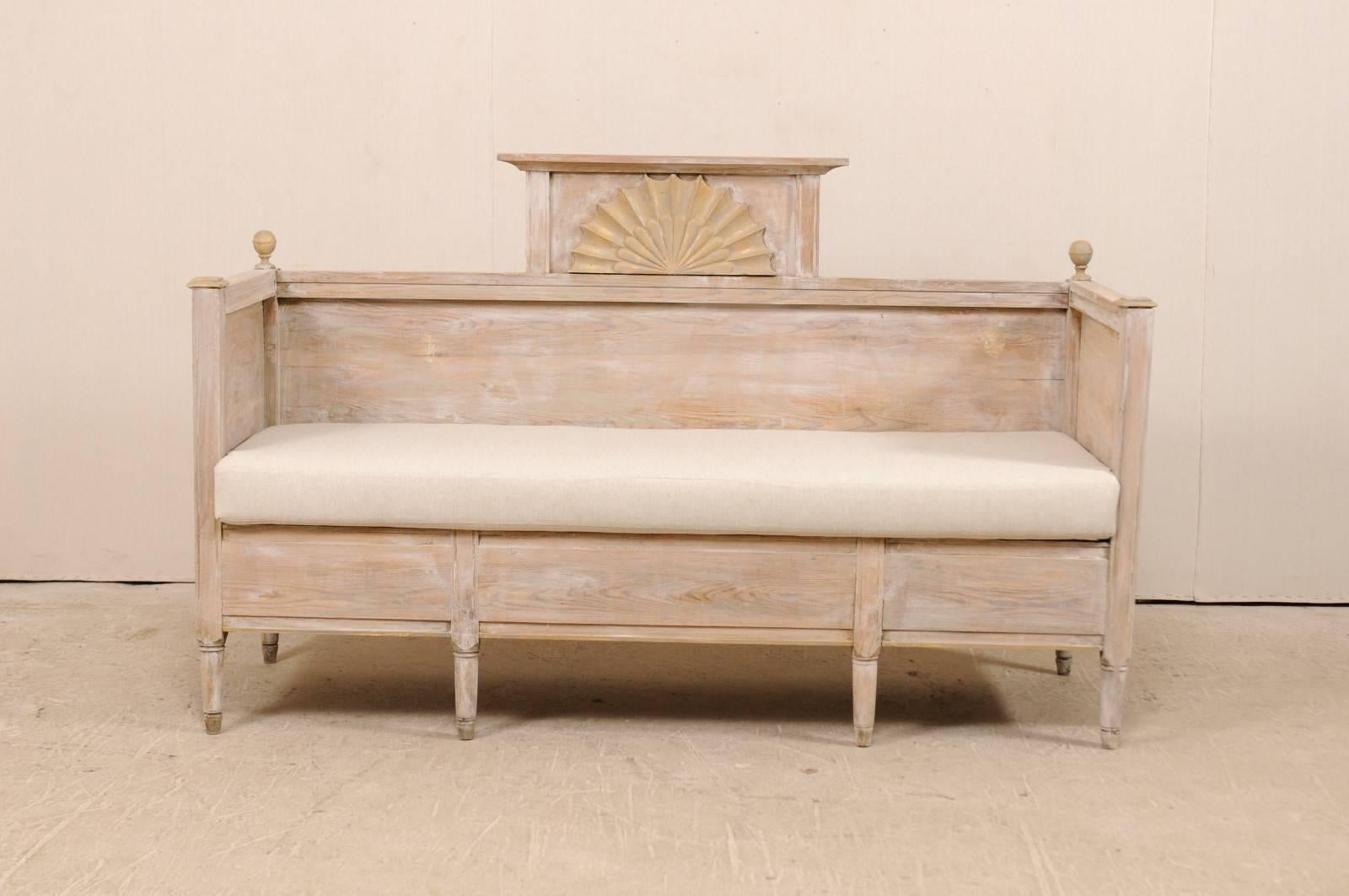 An early 19th century Swedish wood sofa bench. This antique Swedish wood sofa bench features a raised back pediment with a carved fan in it's centre, high arms, and plain skirt. There are ball finials decorating each far side of the sofa back. This