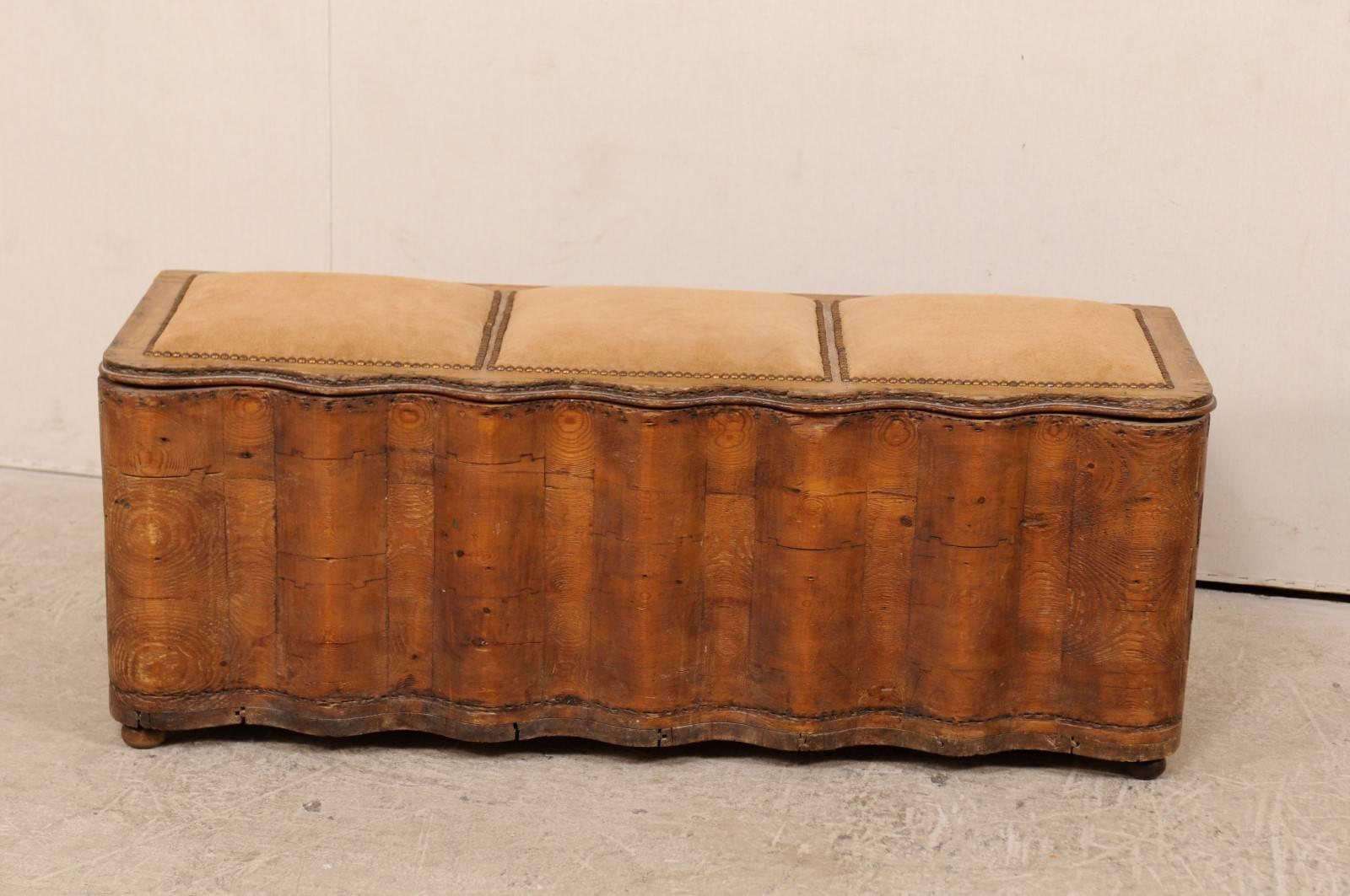 An early 19th century Italian wood bench with storage. This antique Italian bench features a beautifully undulating wood front of vertically carved waves with rounded corners, and plain sides and rear. The top bench seat is suede with nailhead
