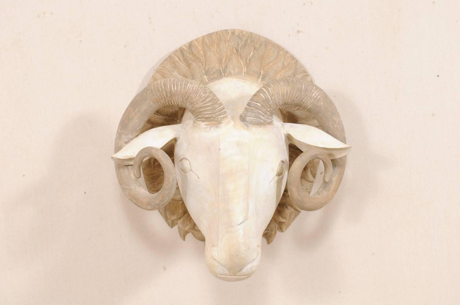 A carved wooden ram's head. This hand-carved ram's head features a forward facing three-dimensional ram with beautifully curled and textured horns, mounted onto a rounded wooden back plate which has been nicely carved and decorated. This ram has