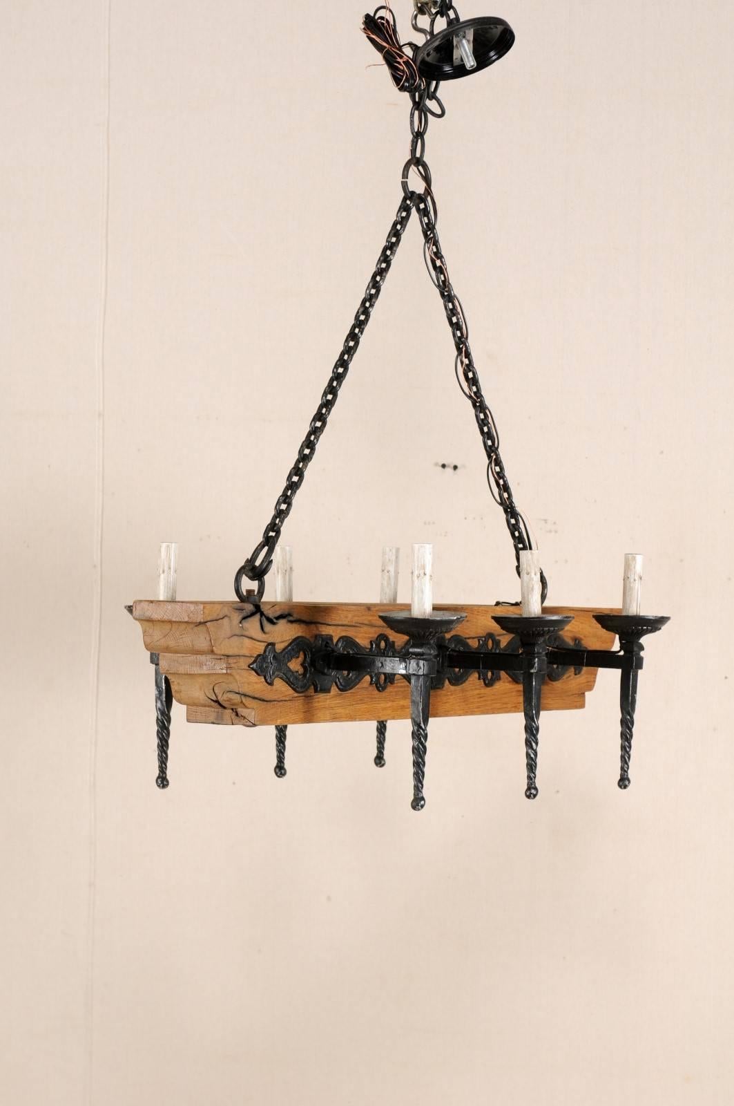 A French six-light wooden beam and iron arms chandelier from the mid-20th century. This vintage French chandelier has a central wooden beam with six torch-style iron arms, three at each opposing side. The six torch light arms with spiralized posts