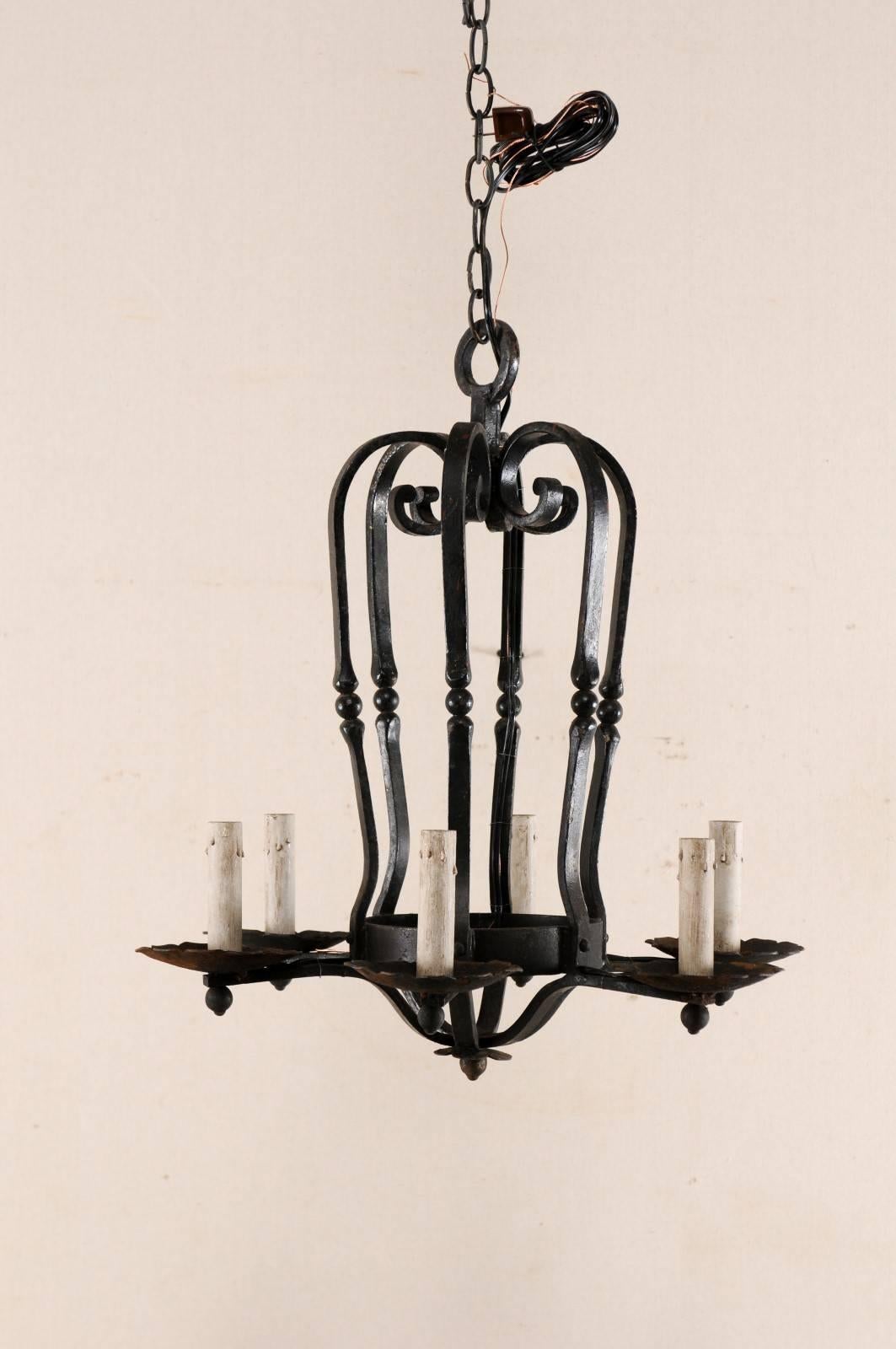 A vintage French six-light black iron chandelier. This French light fixture from the mid 20th century features an elegantly oblong caged center body with scrolled motif at it's top and iron accent beads decorating each post. There are six arms which